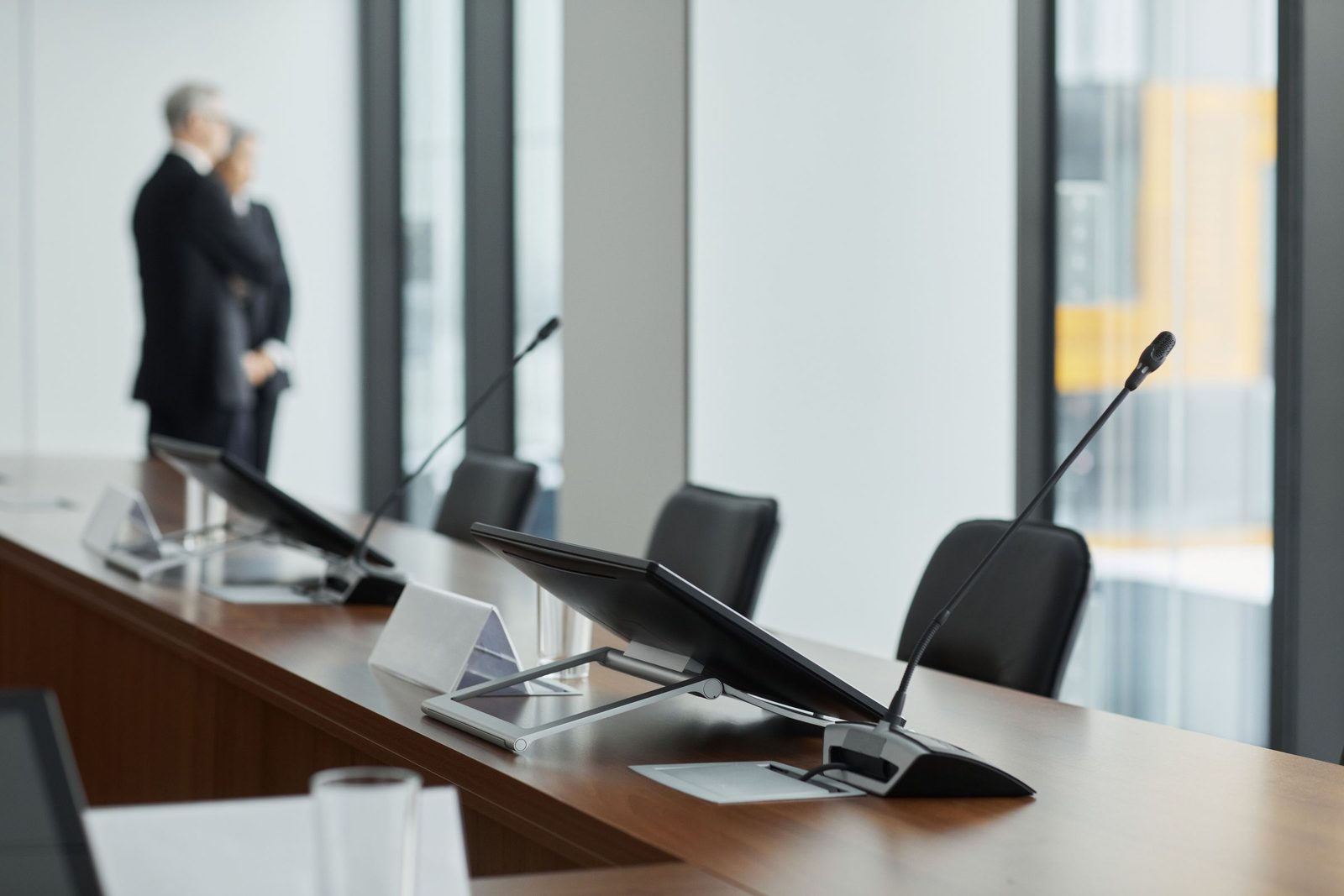 Microphones and monitors set out along an empty wooden conference table.