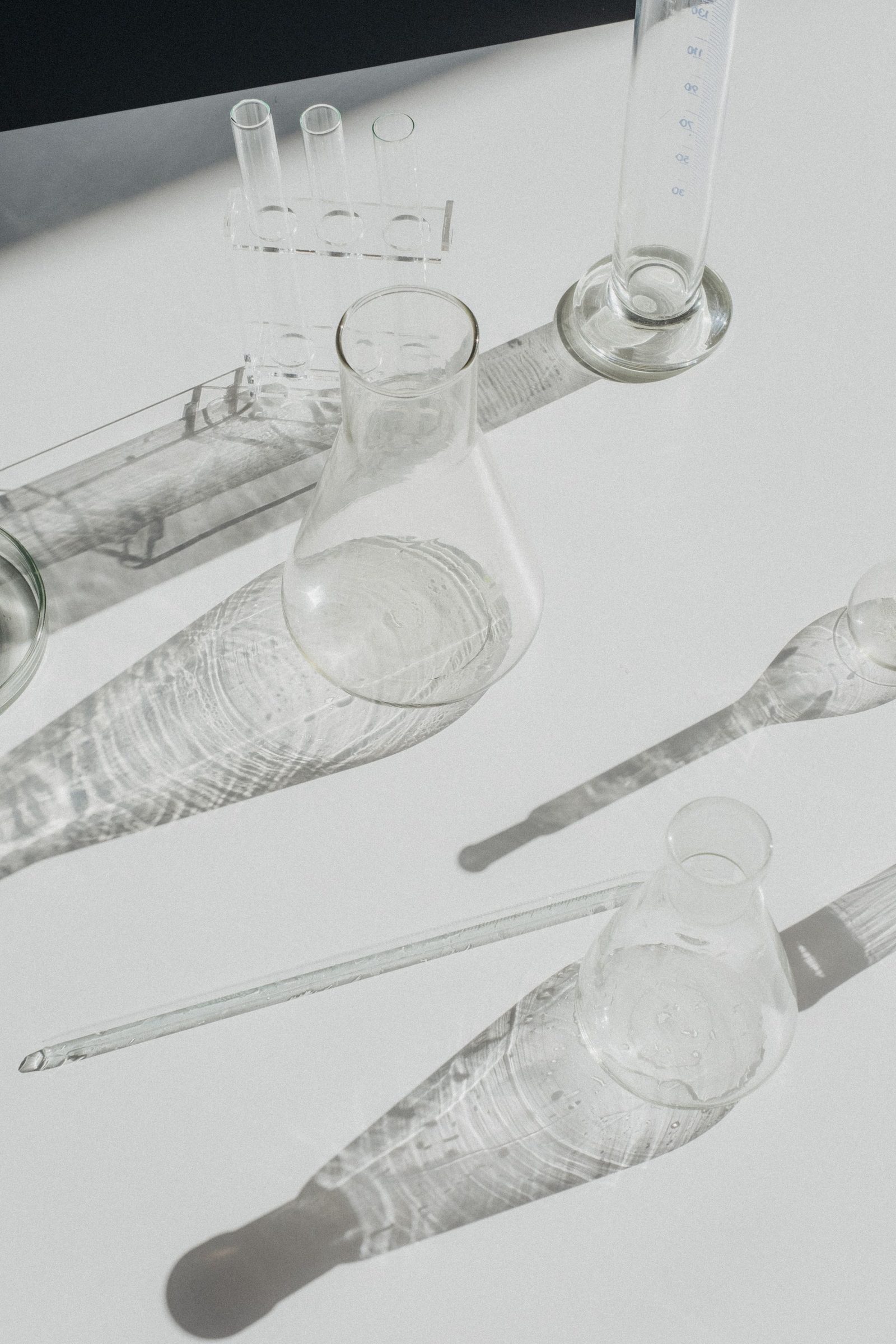 Laboratory glassware casting long shadows across a white surface.