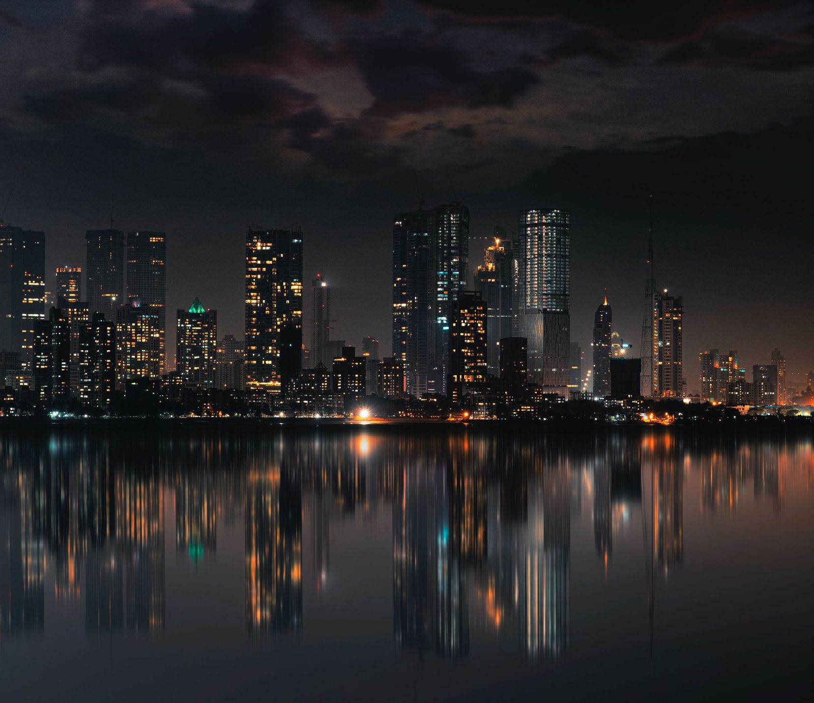 The Mumbai skyline at night with lit towers reflected in still water.