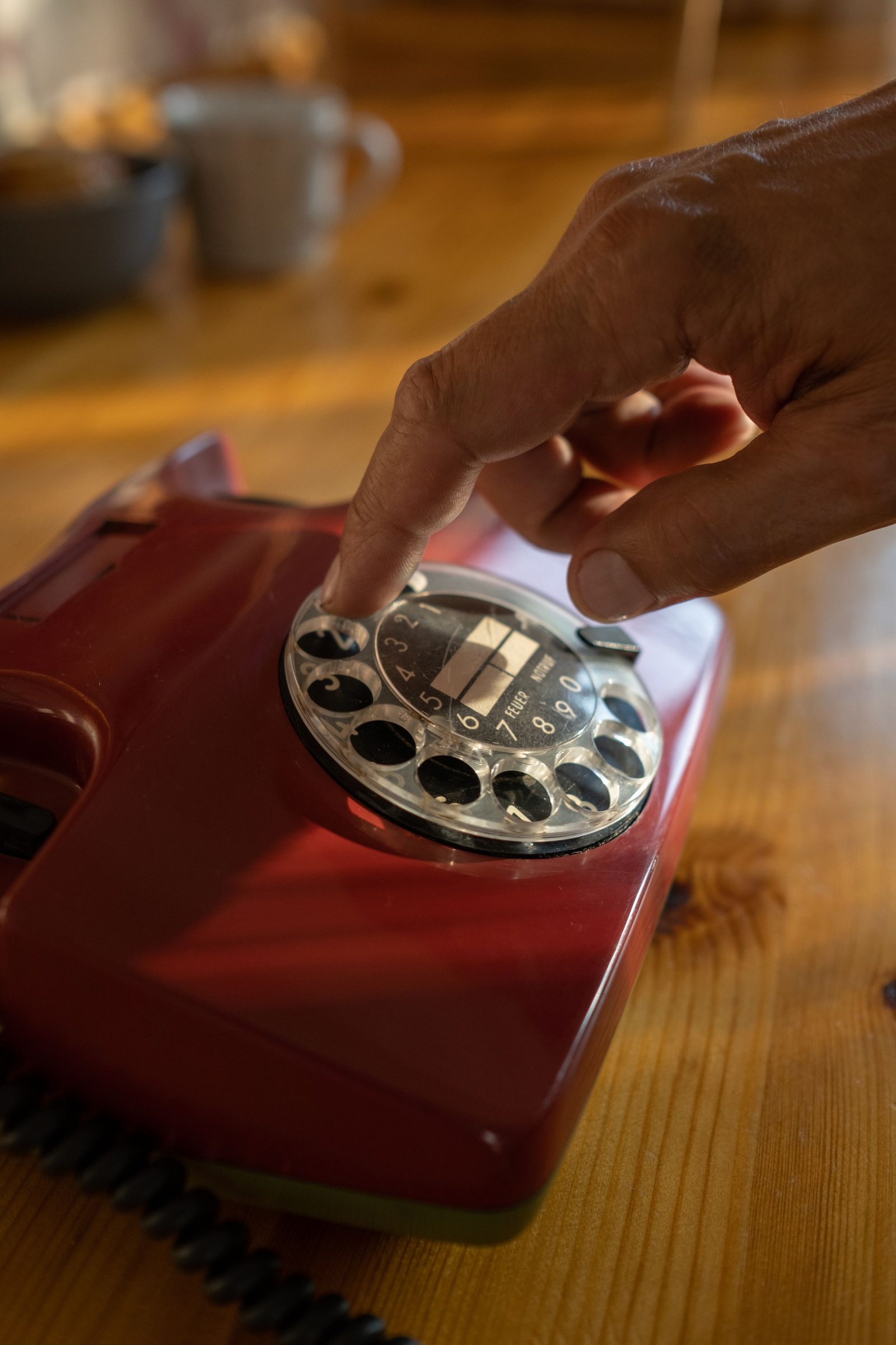 A hand dialling a red rotary telephone in close-up.