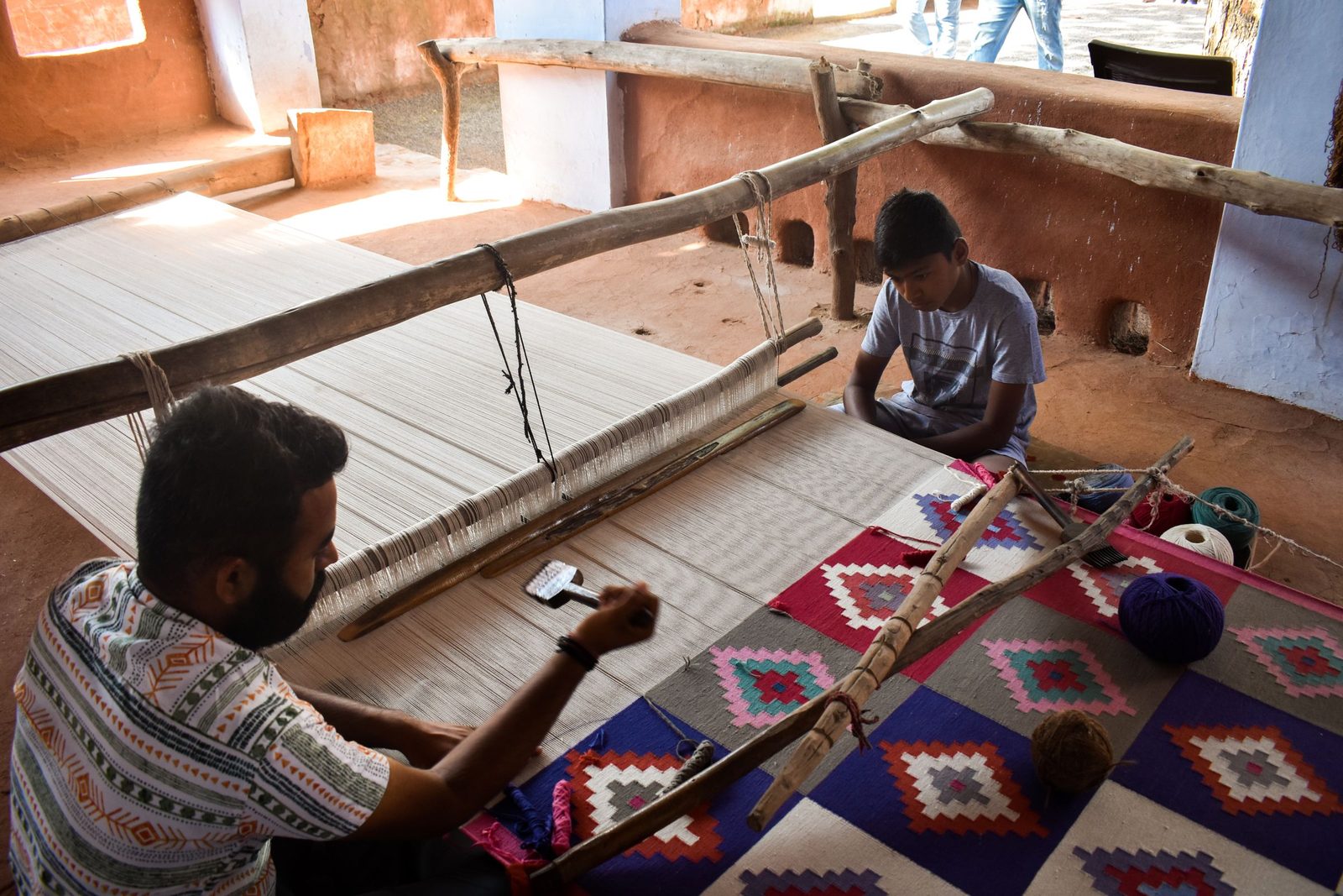 An artisan and a child weave a coloured carpet on a handloom in a Jodhpur workshop.