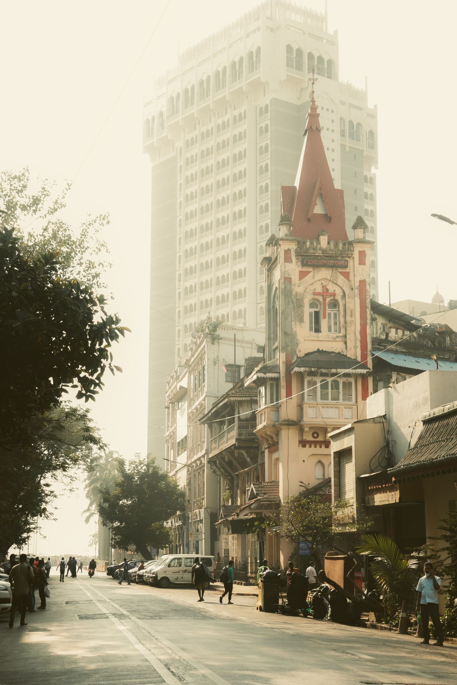 Old stone buildings line a quiet Mumbai street in soft morning light with a tower beyond.