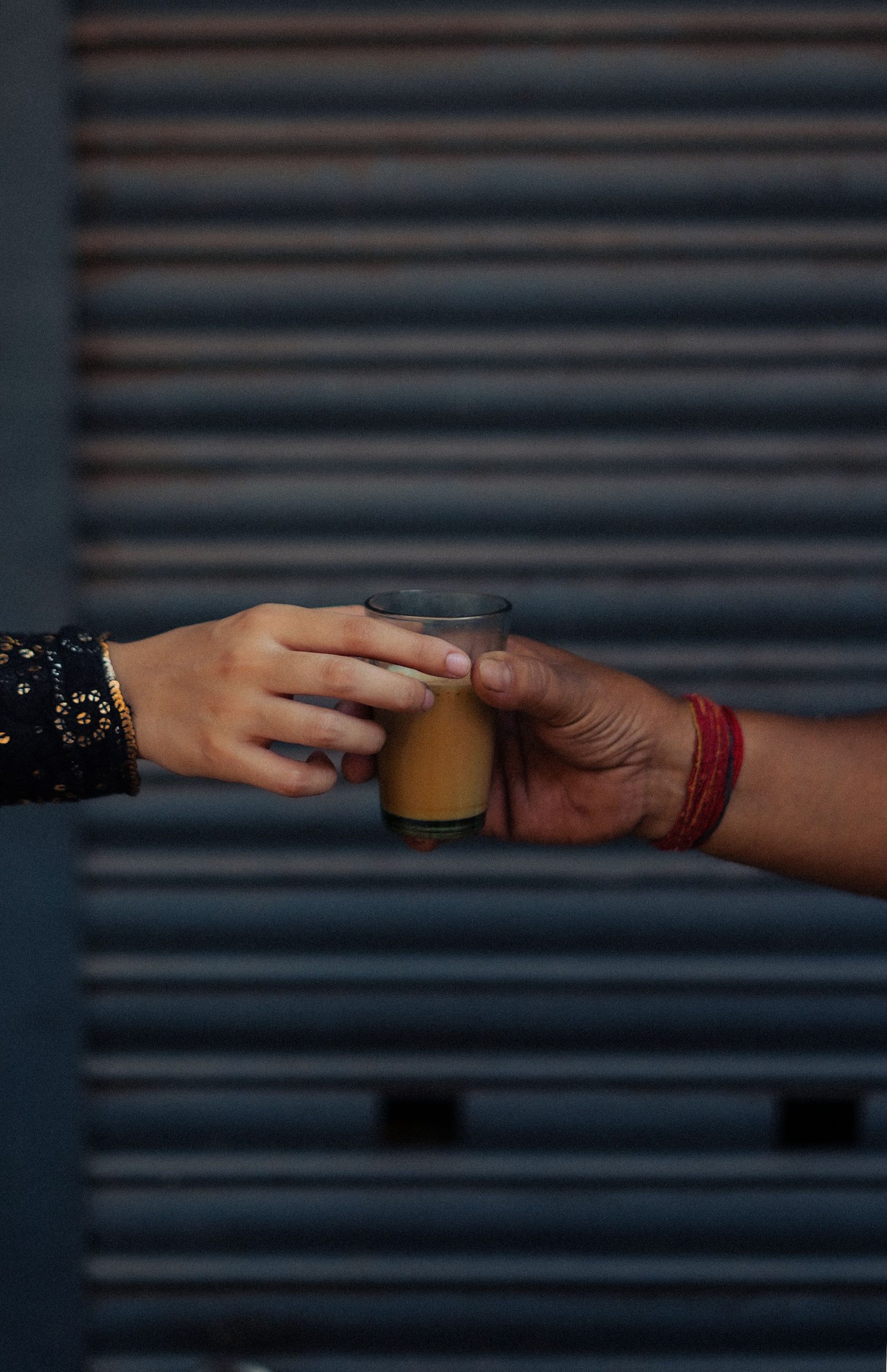 Two hands pass a glass of tea between them.
