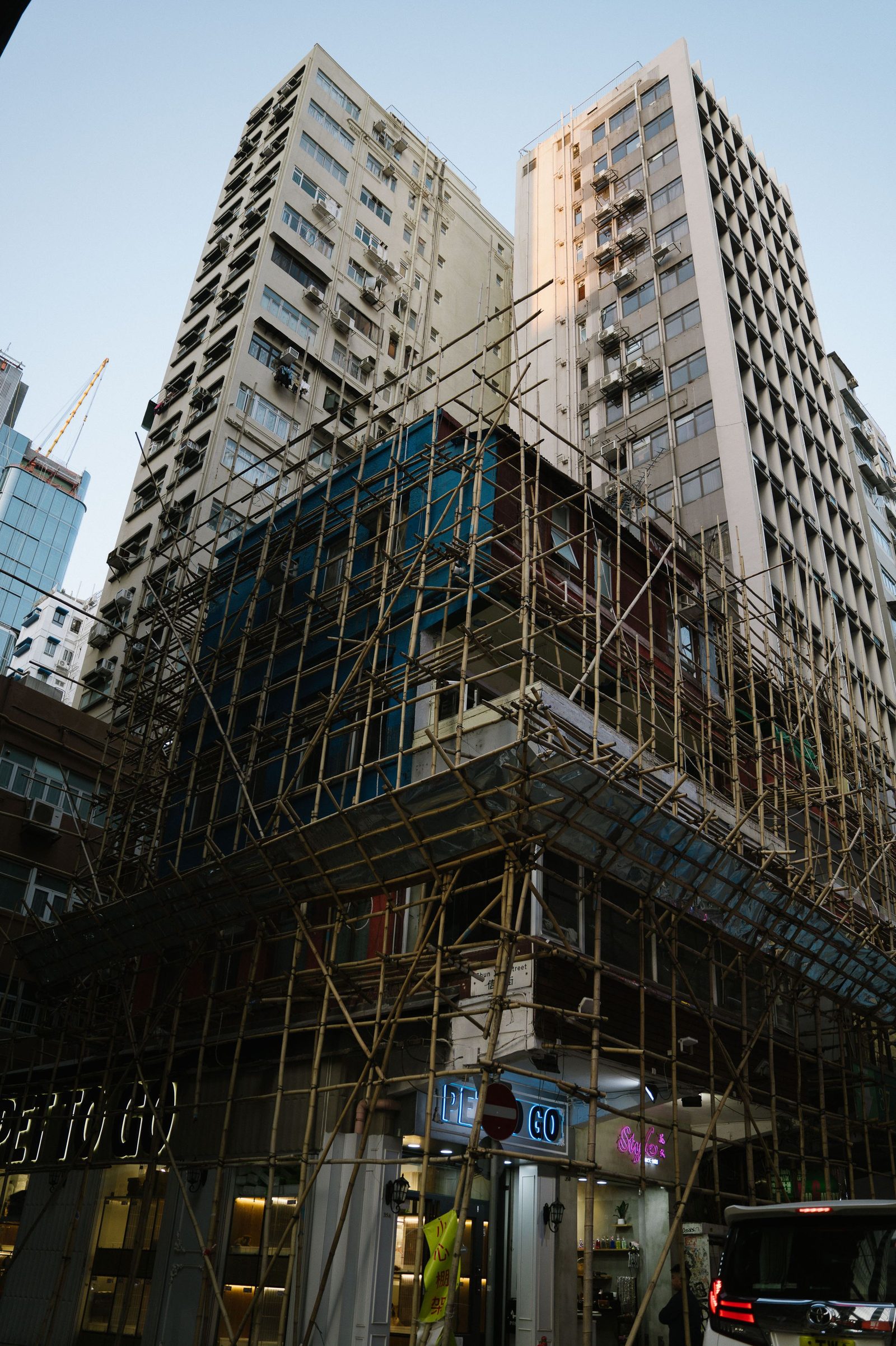 High-rise buildings wrapped in bamboo scaffolding at dusk.