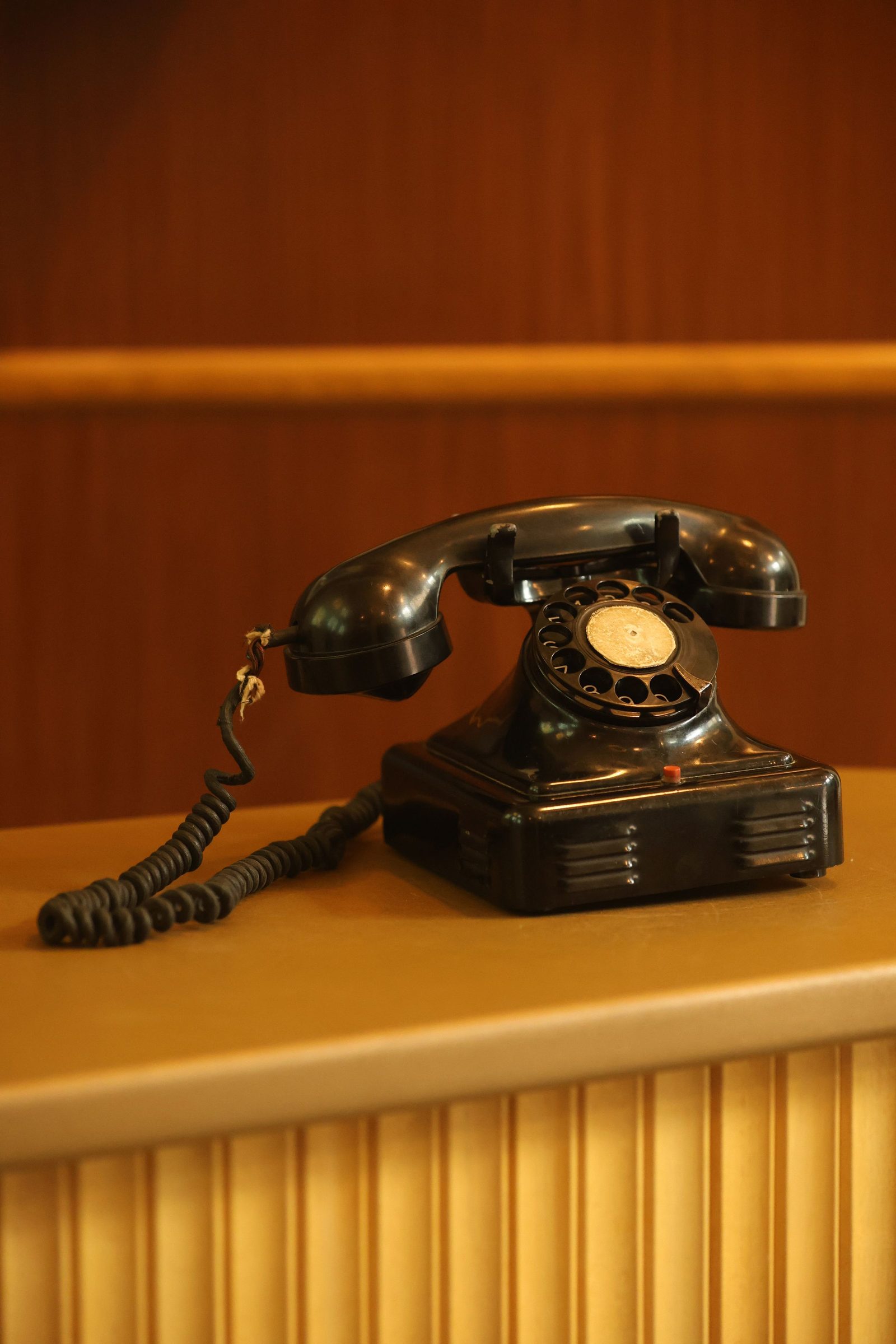 A black rotary dial telephone on a wooden desk.