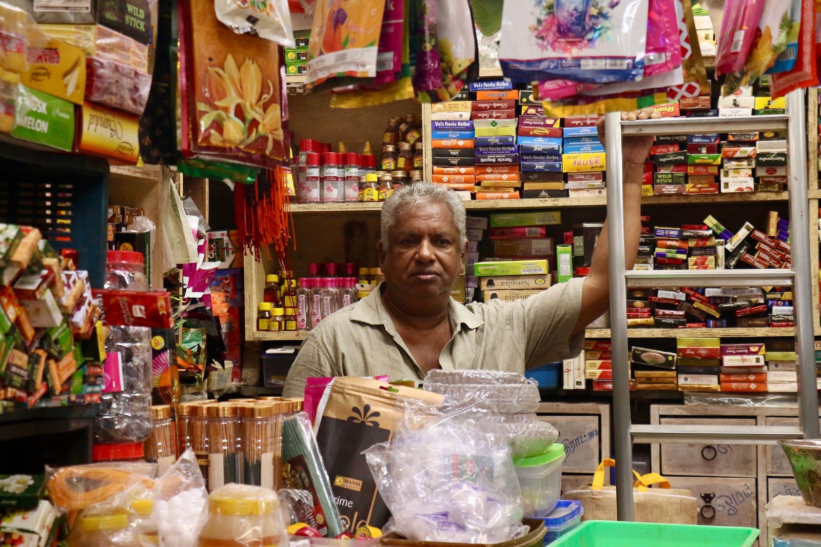 A man works among crowded shelves inside an Indian grocery store.