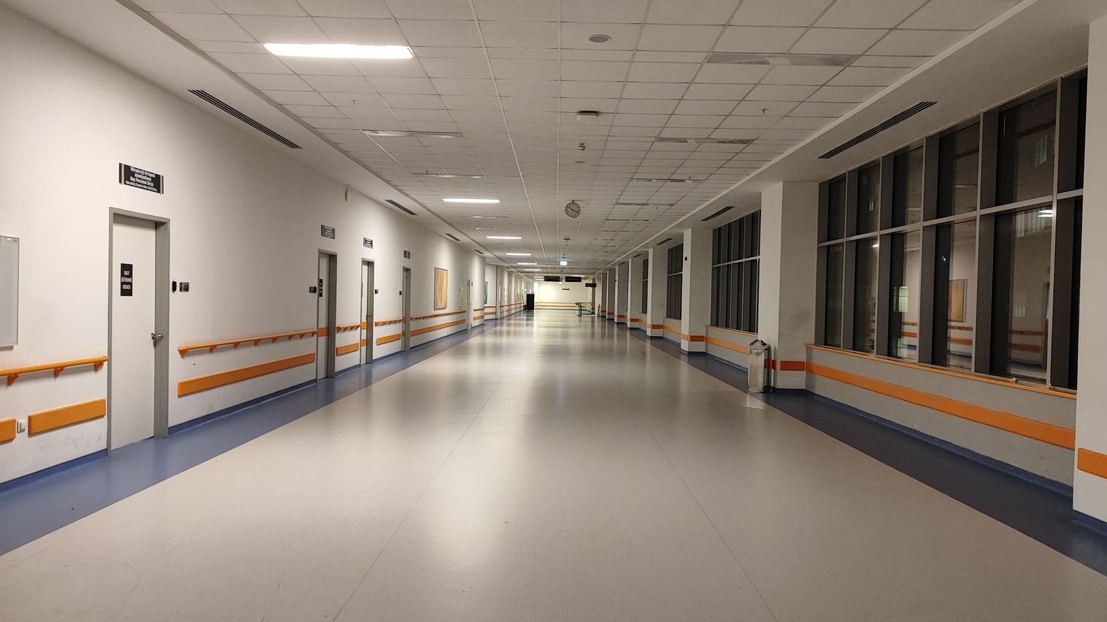A long empty hospital corridor with a polished floor and windows along one side