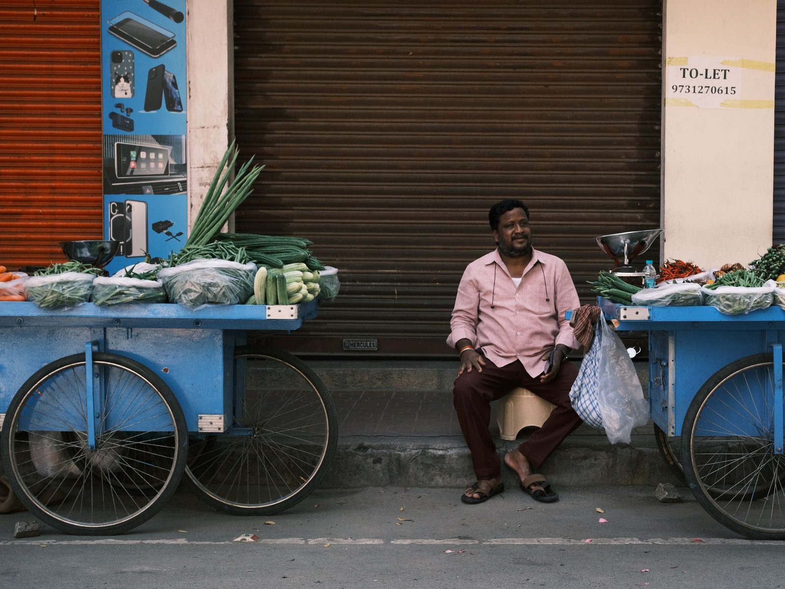 A street vendor sits beside his vegetable cart on a quiet Bengaluru street.
