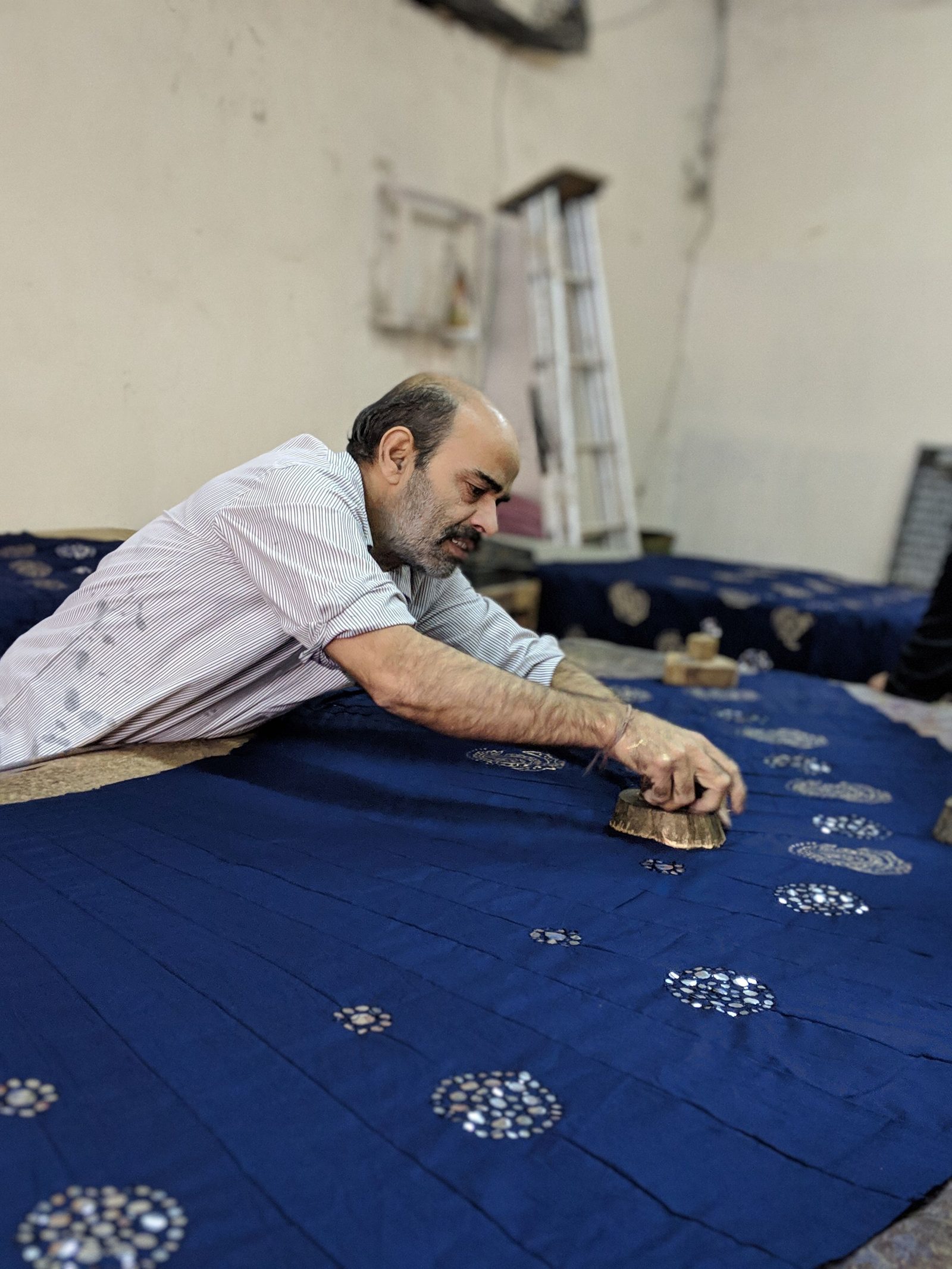 An artisan presses a wooden block onto blue fabric in a Jaipur printing workshop.