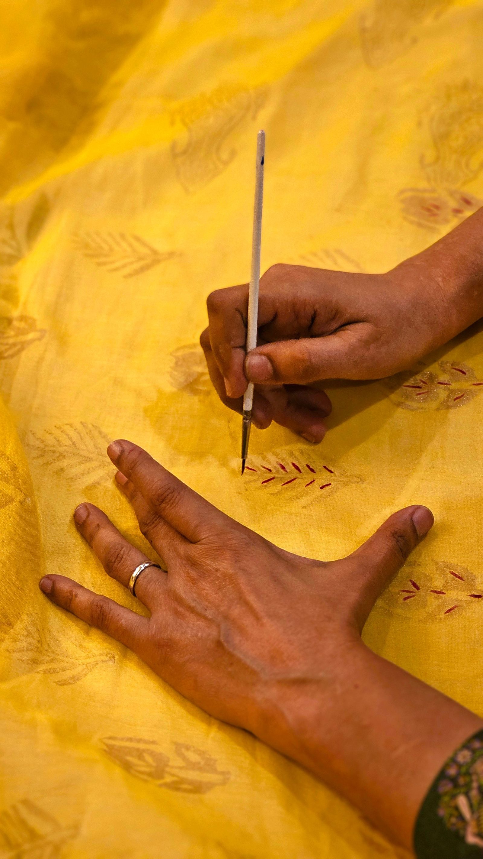 A hand block print leaves a repeating pattern on yellow fabric.