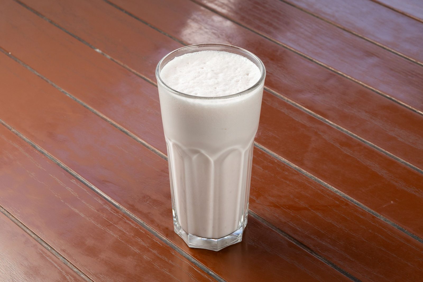A vanilla milkshake in a tall glass on a wooden table.