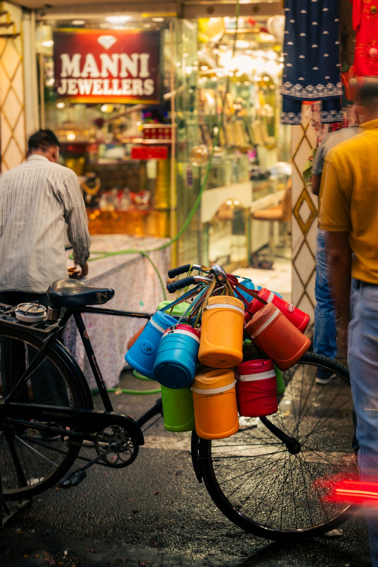 Steel tiffin carriers hang in a stack from a bicycle on a busy street in Ludhiana.