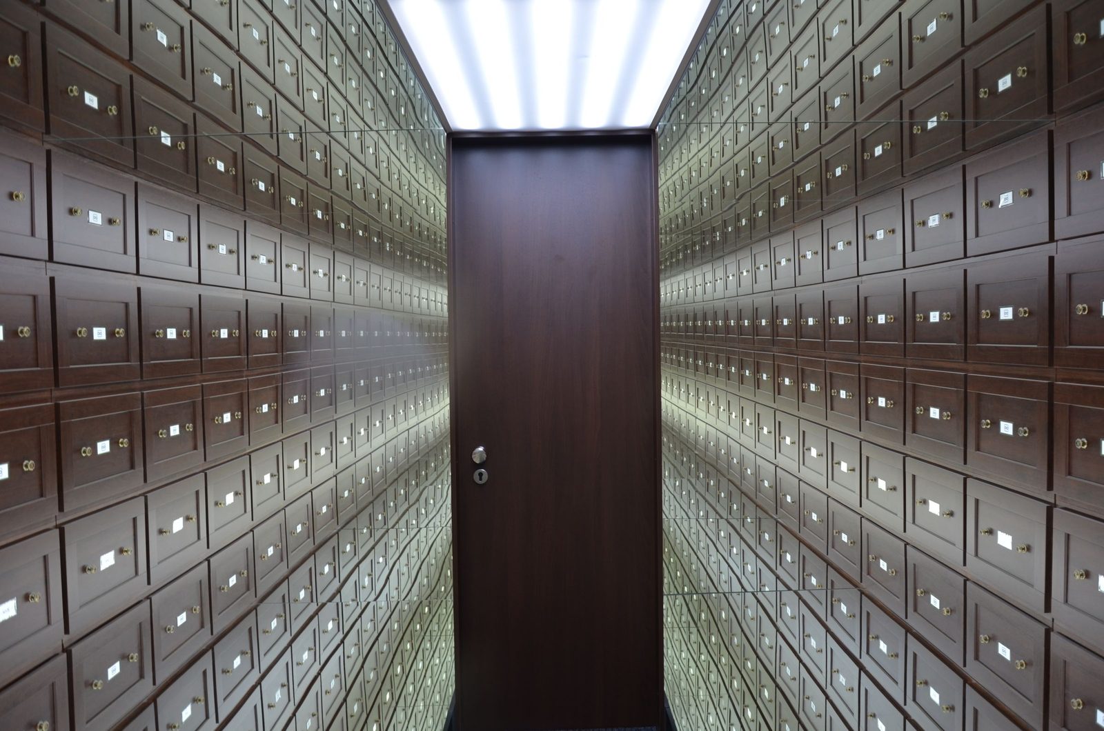 Rows of wooden lockboxes line the walls of a vault around a central wooden door.
