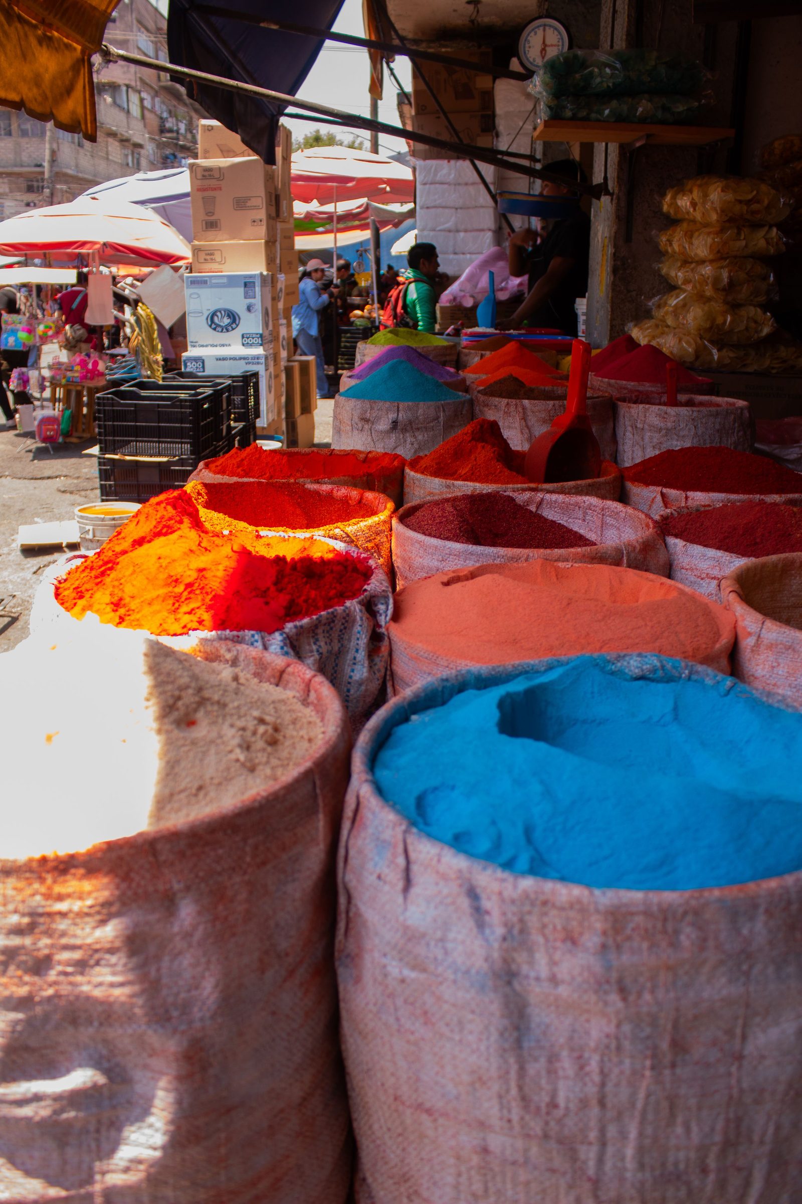 Open sacks of brightly coloured powders at an outdoor market.