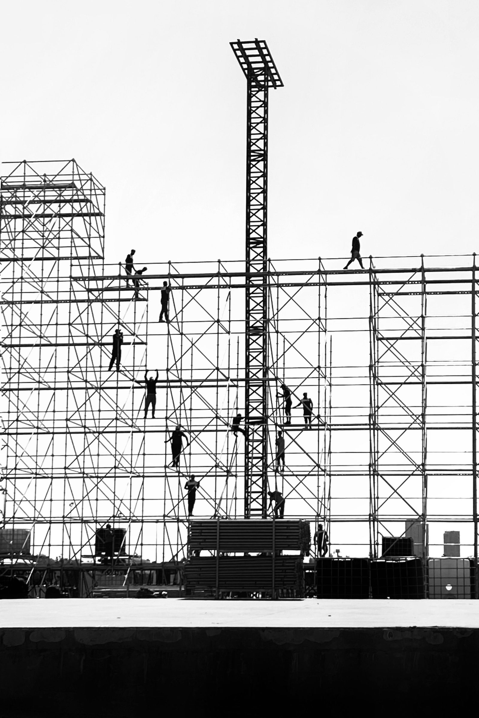 Workers silhouetted against a pale sky as they climb a tall steel scaffold.