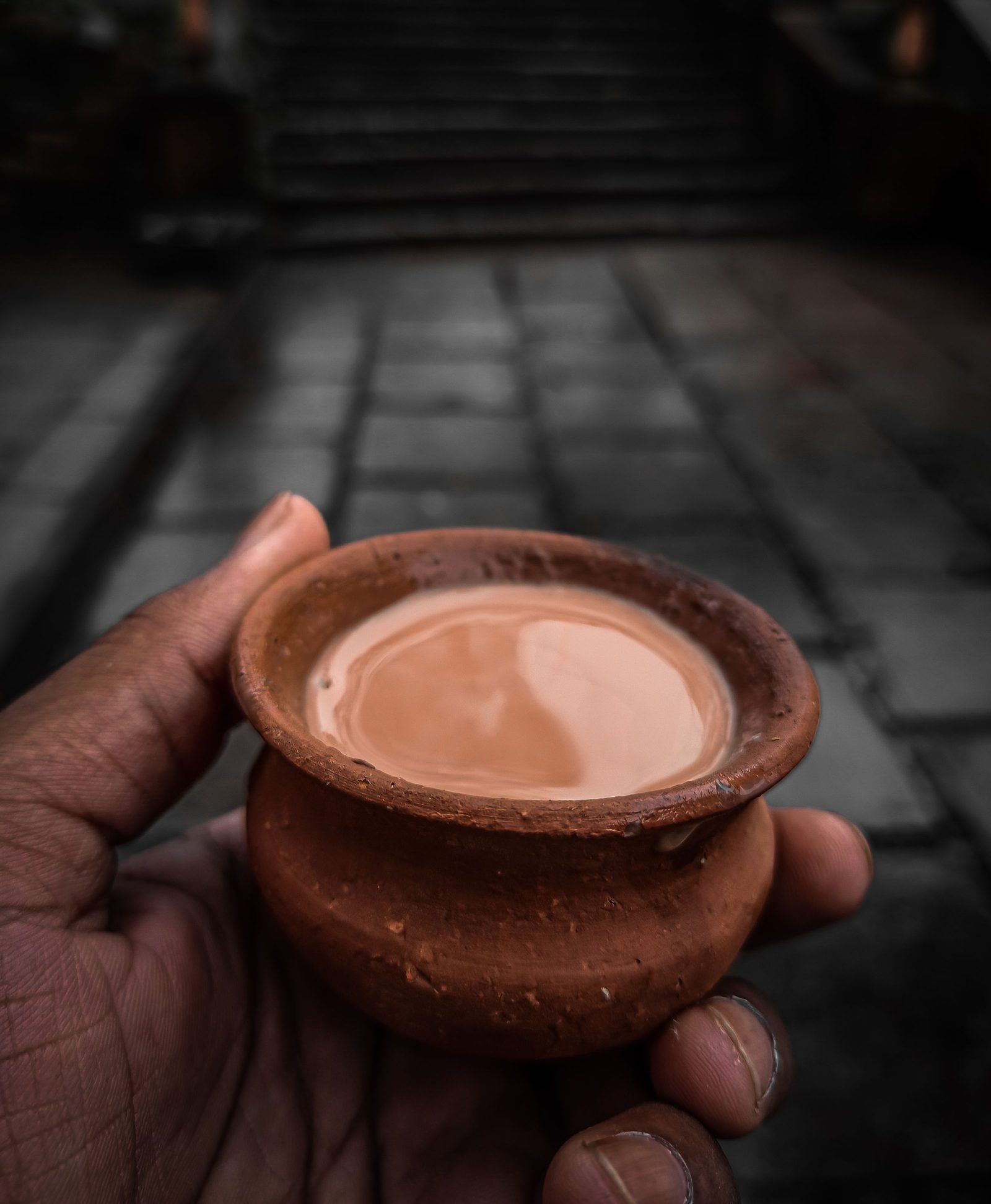 A hand holds a small clay cup of masala chai outdoors.