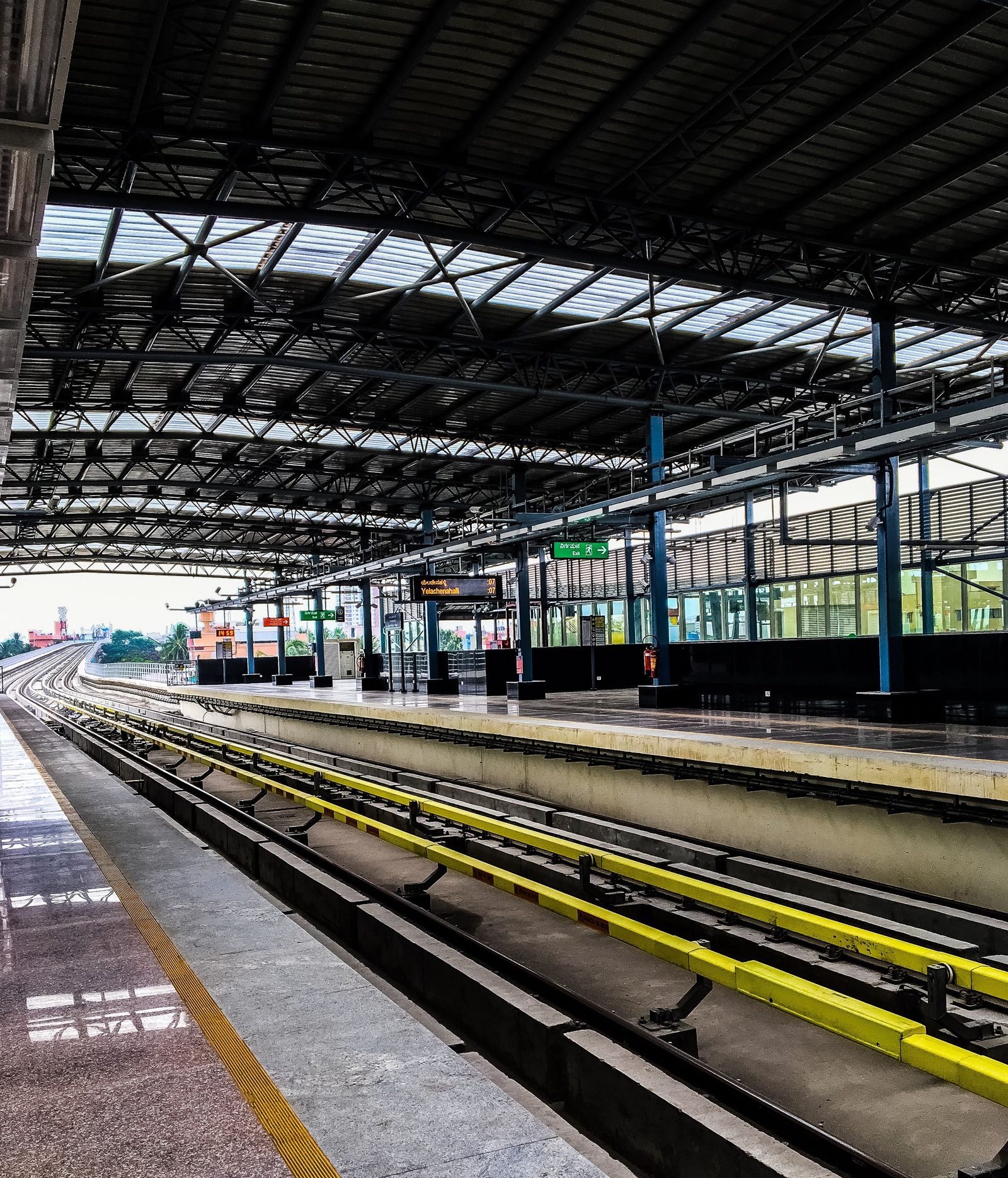An empty railway platform in Bengaluru runs beside bare tracks under a long canopy.