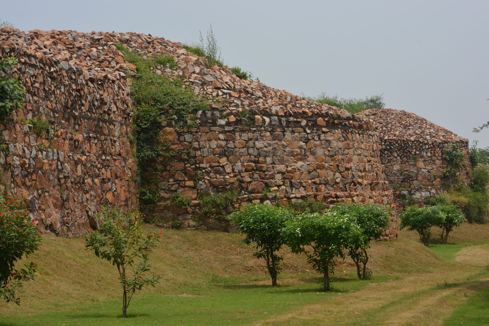 Weathered rubble-stone fortification walls run across a green lawn in New Delhi.