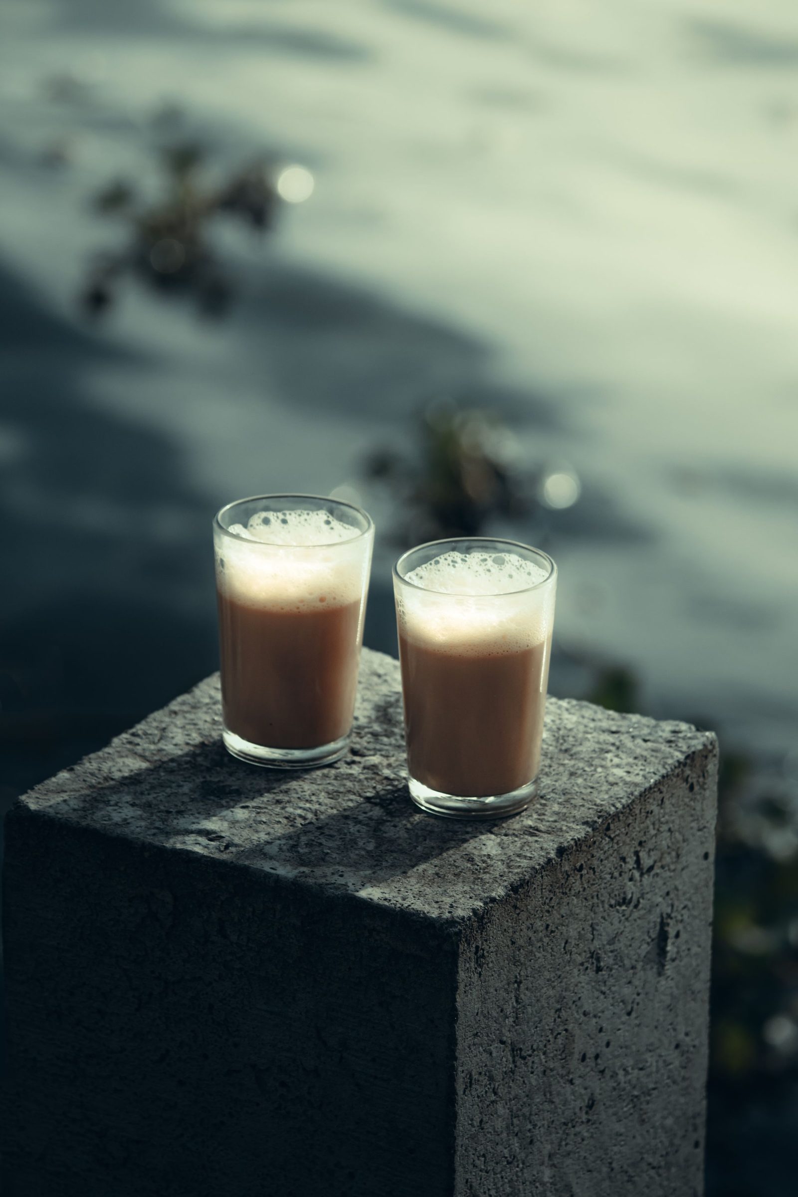 Two glasses of chai stand on a stone beside the water in Alappuzha, Kerala.