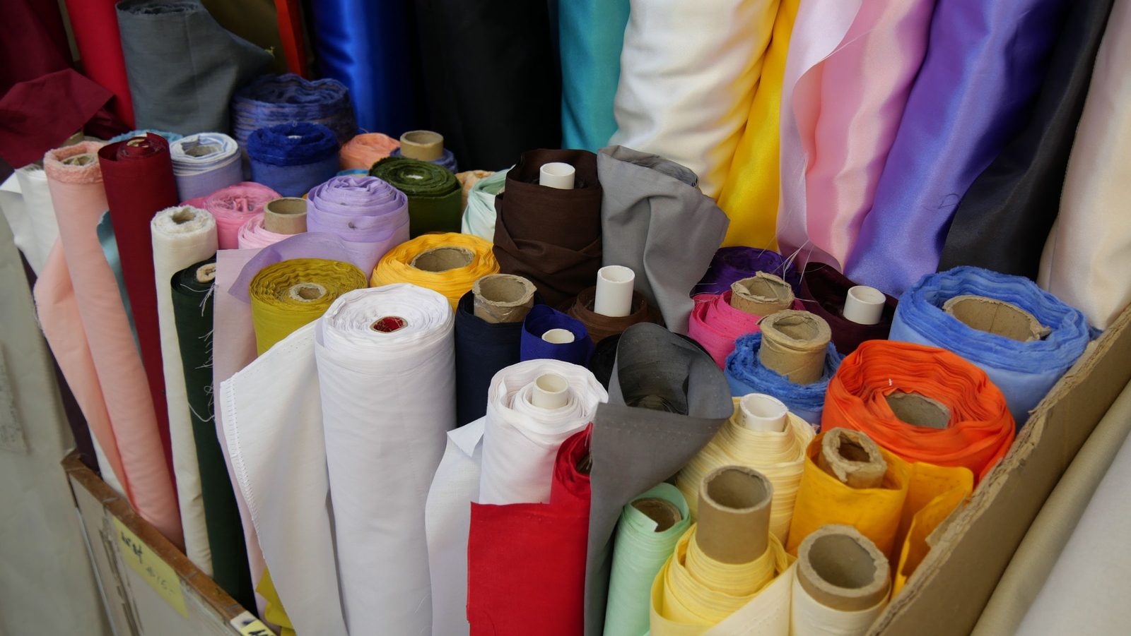 Rolls of fabric in many colours lie stacked in a textile store.