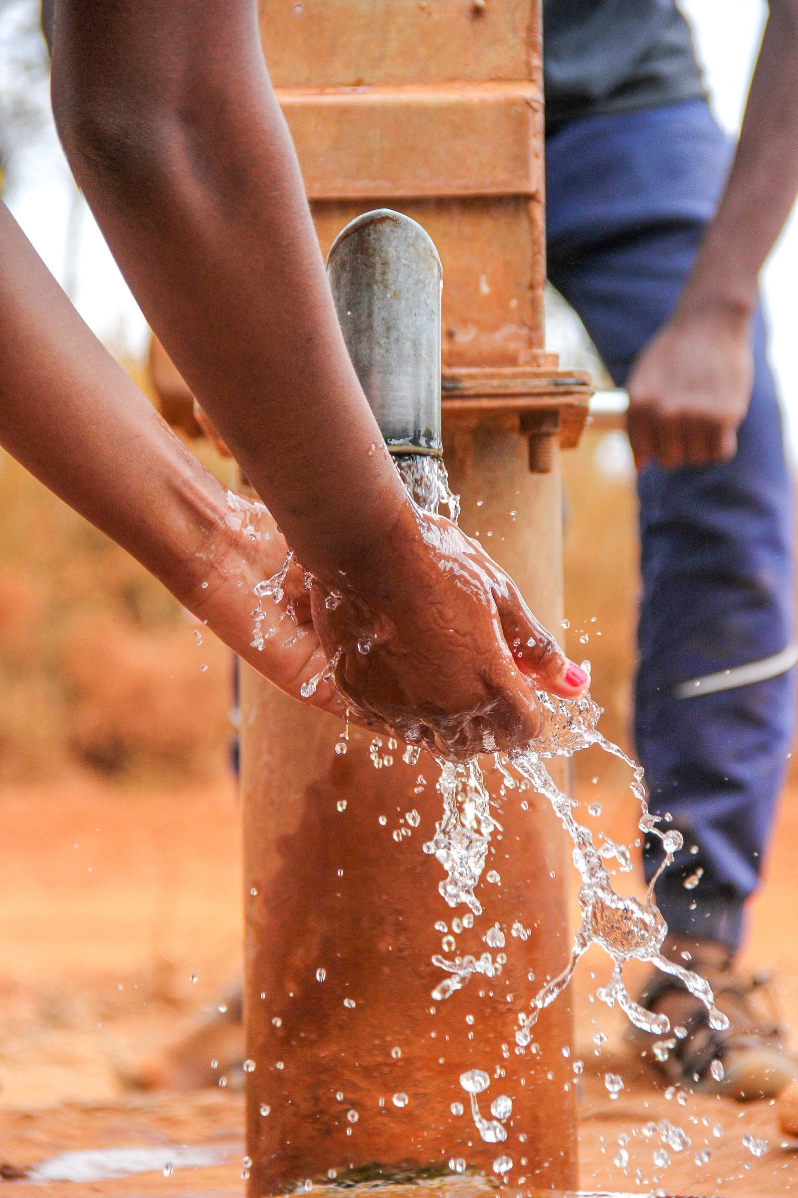 Hands being washed under a rural hand pump.