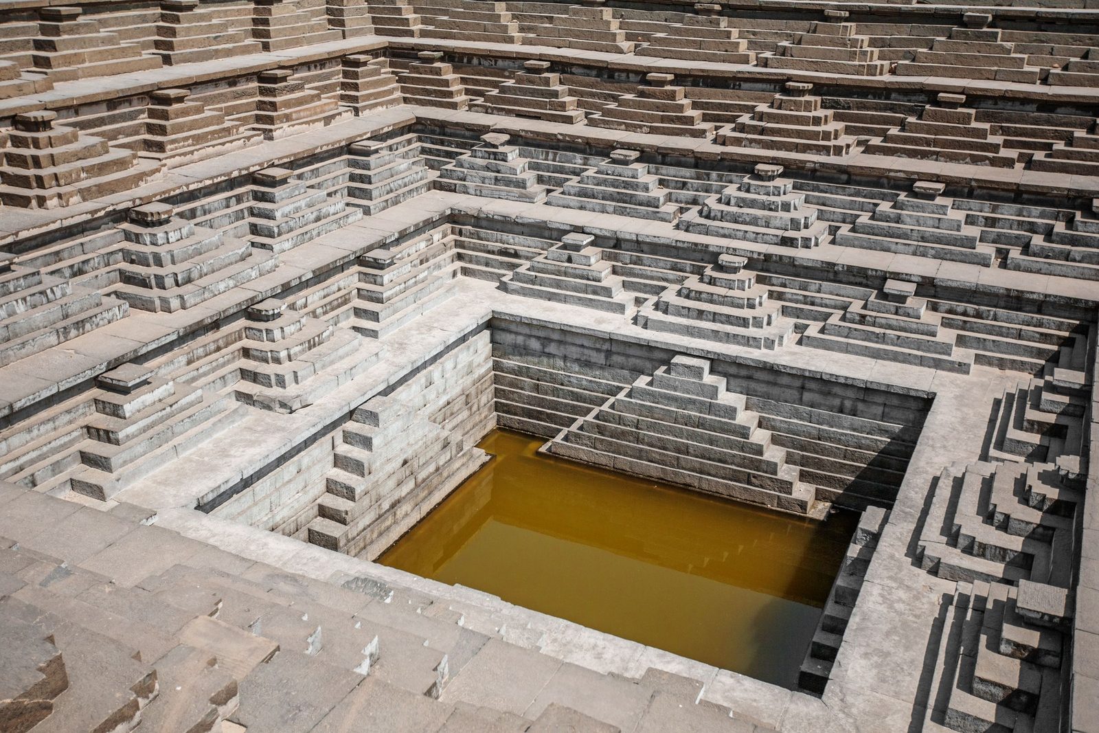 A stone stepwell in Hampi holds still water at its base.