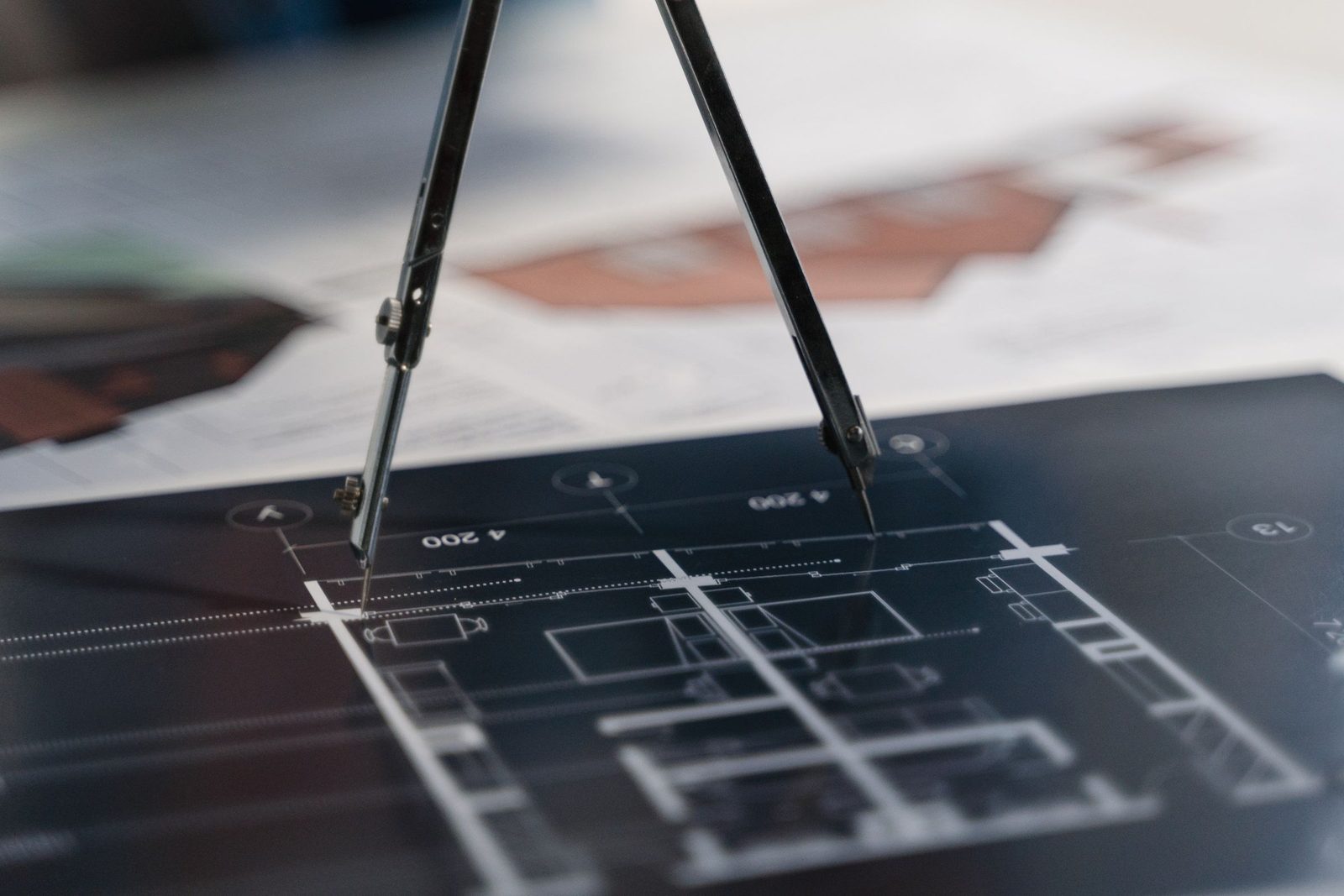 A drawing compass rests on a sheet of architectural plans.