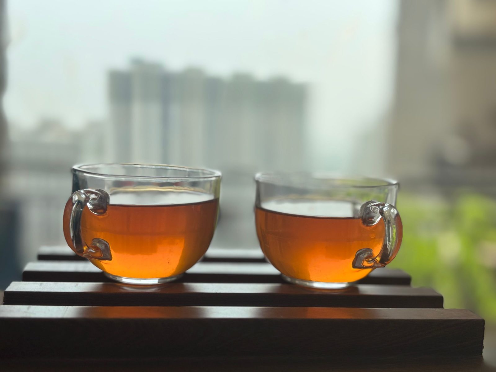 Two glasses of tea stand on a ledge in Noida with the city blurred behind them.