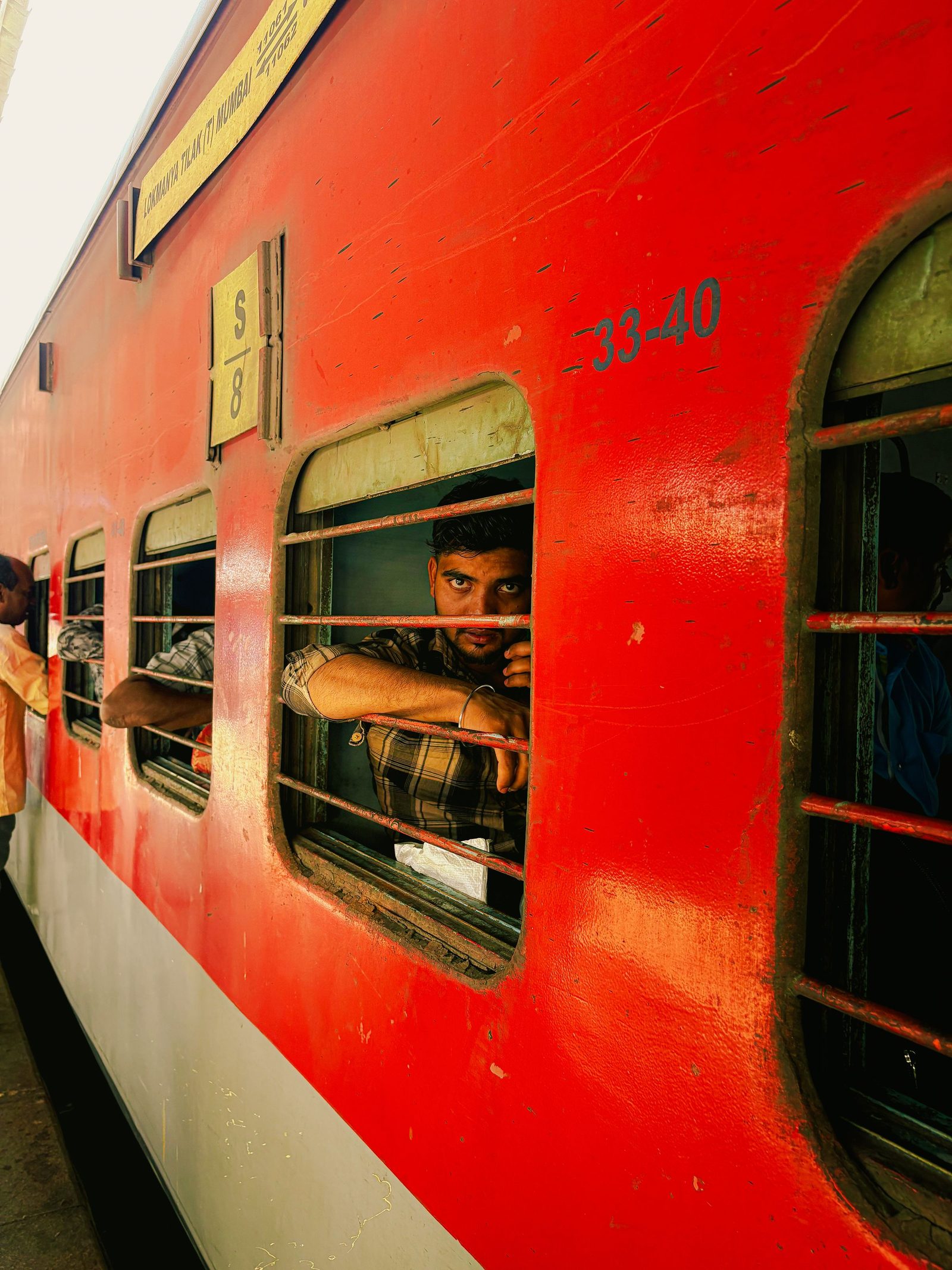A passenger looks out of the barred window of an Indian railway carriage.