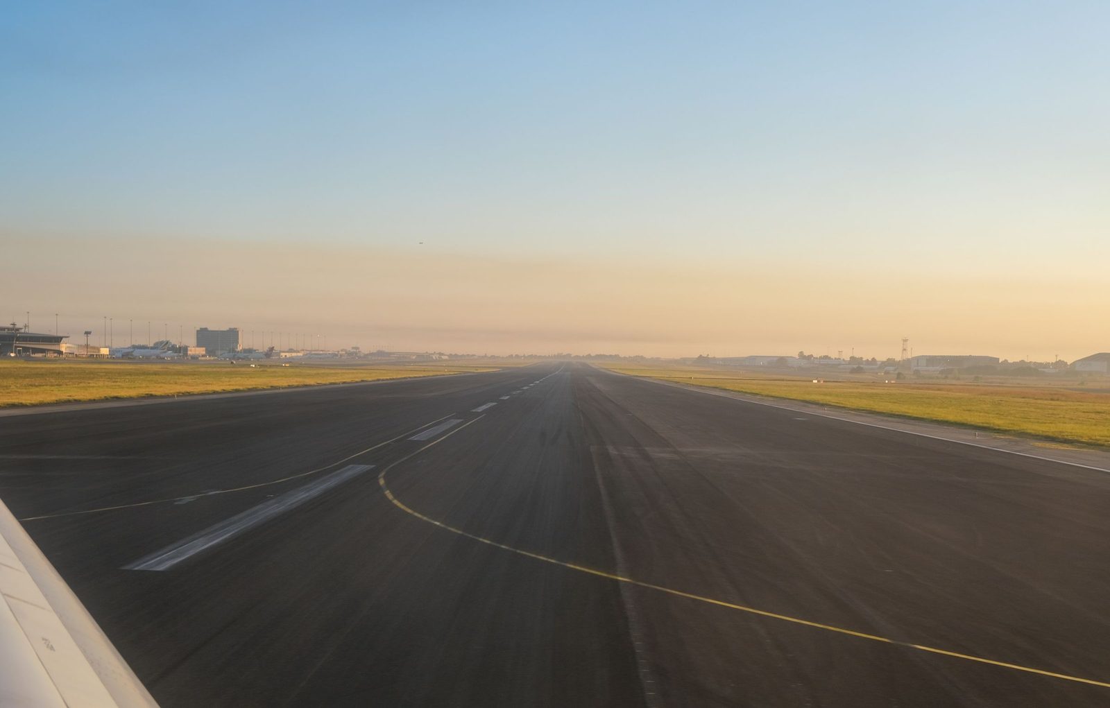 An empty airport runway at sunrise with airport buildings in the distance.