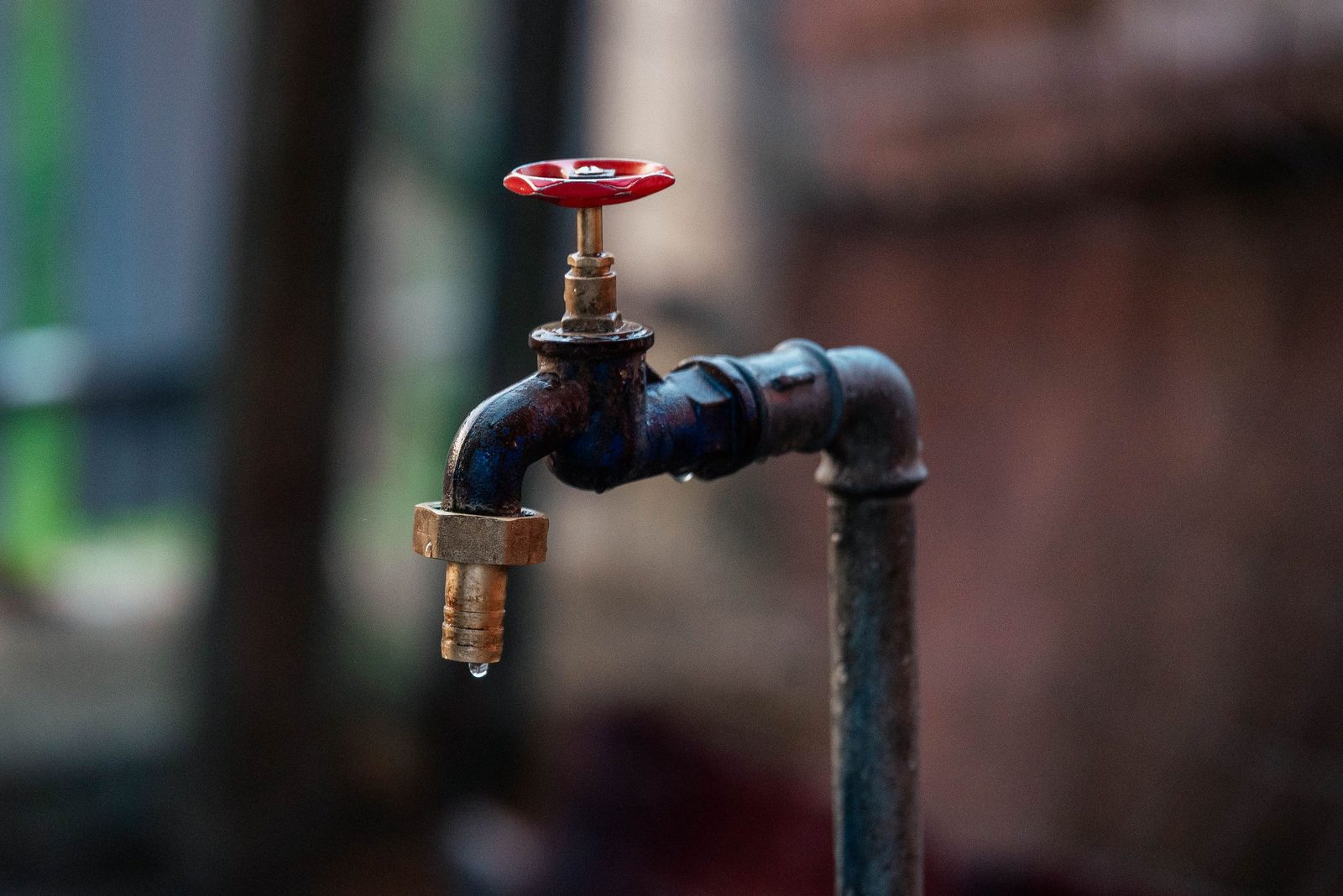 A single drop falls from a rusty outdoor tap.