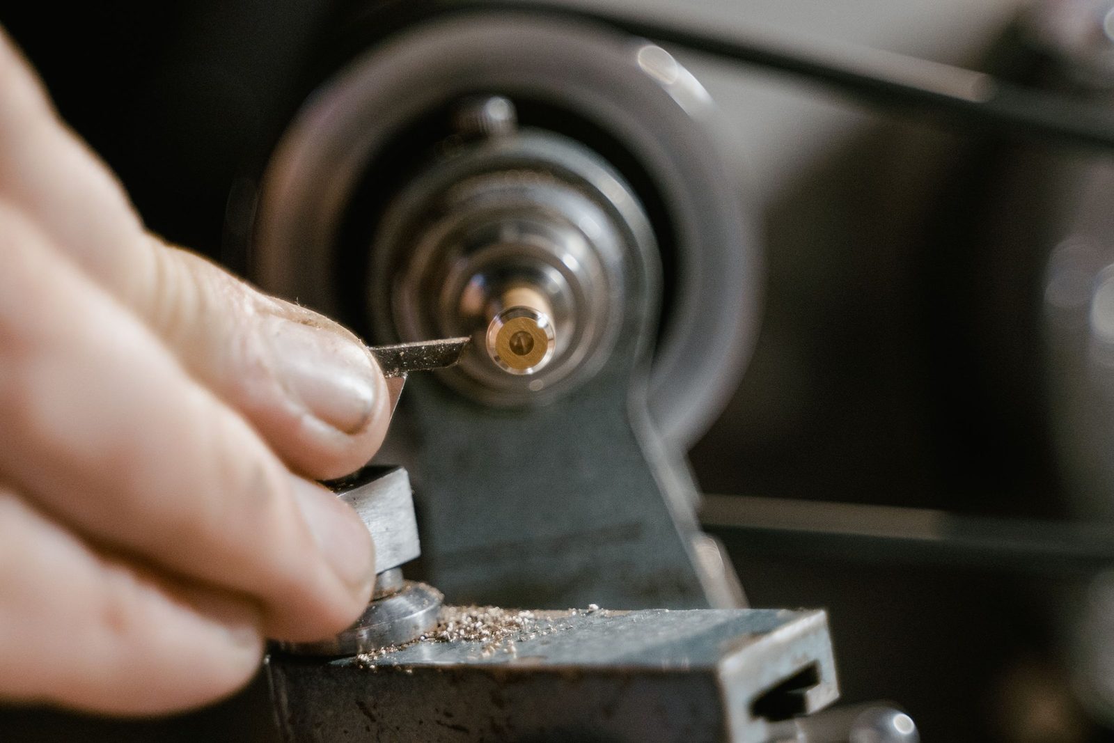 Hands setting a cutting tool against a metal part on a lathe.