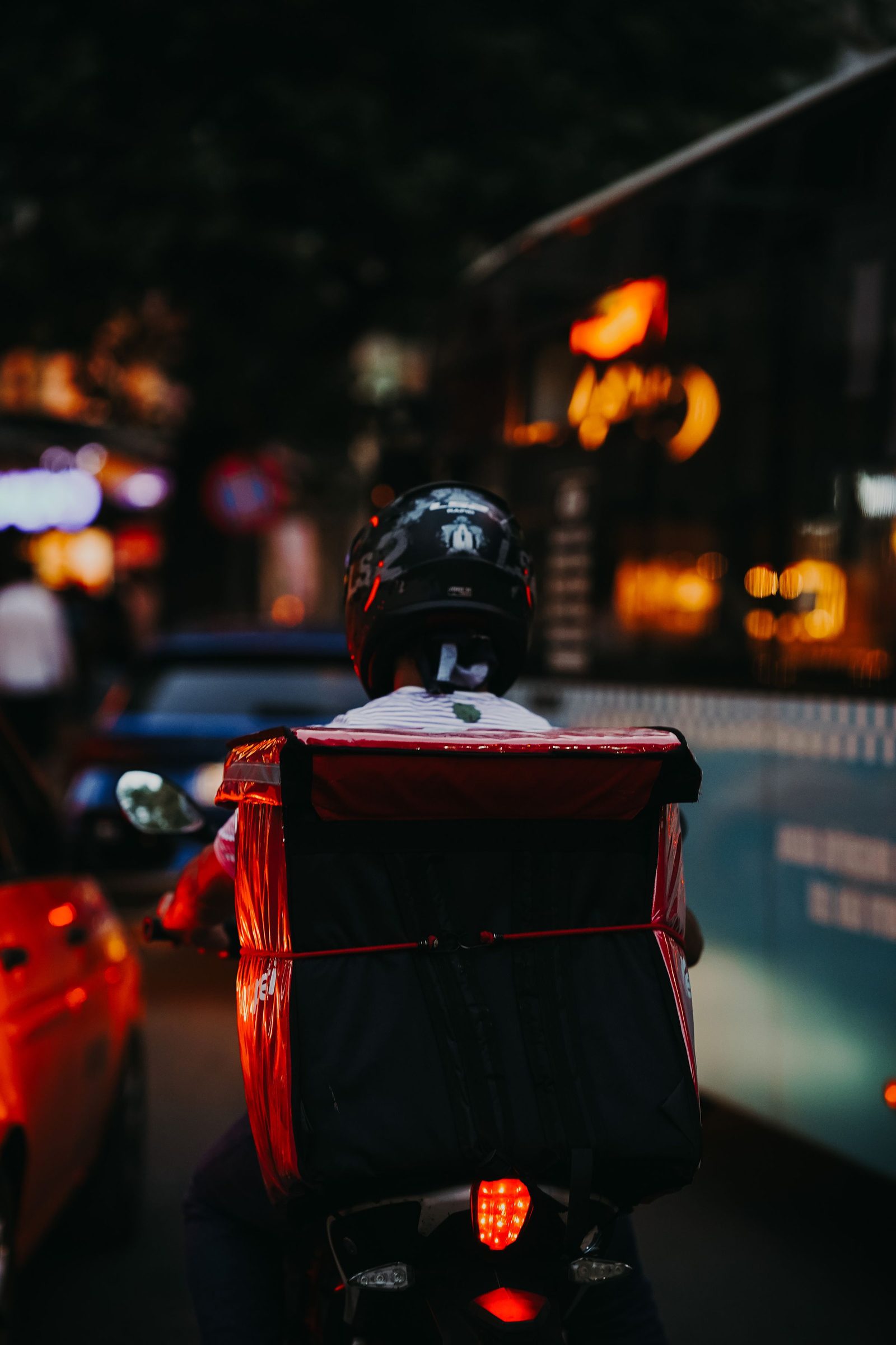 A delivery rider on a motorbike is silhouetted on a city street in the evening.