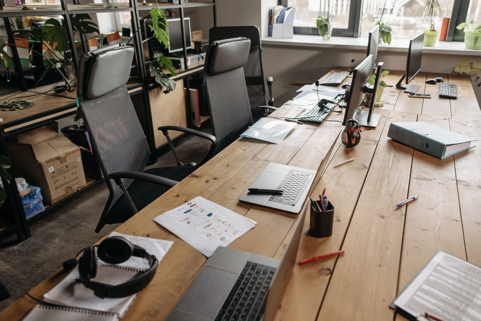 Wooden desks with laptops and empty chairs fill a quiet co-working office.