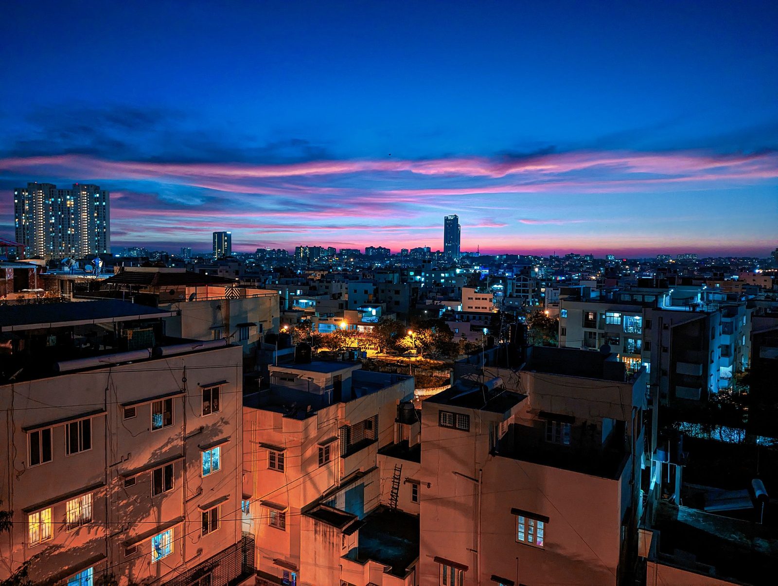 An aerial view of Bengaluru at dusk with lit buildings under an orange sky.