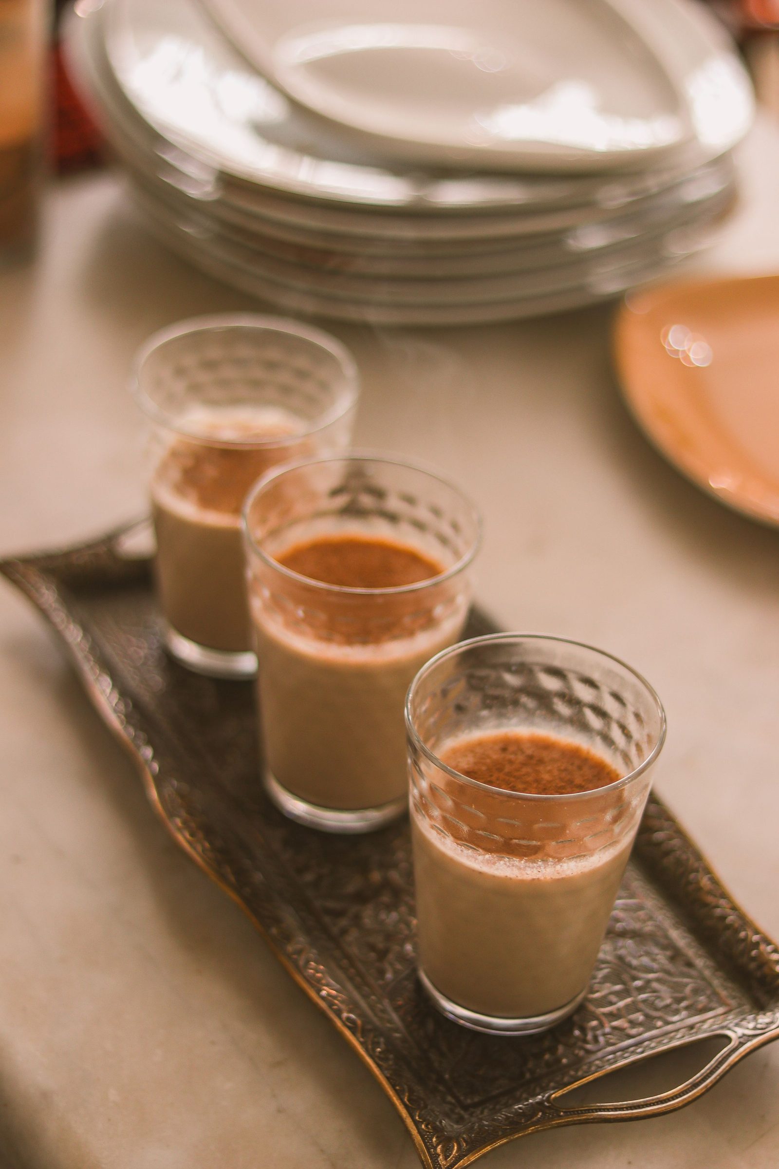 Three glasses of chai on a tray in afternoon light.
