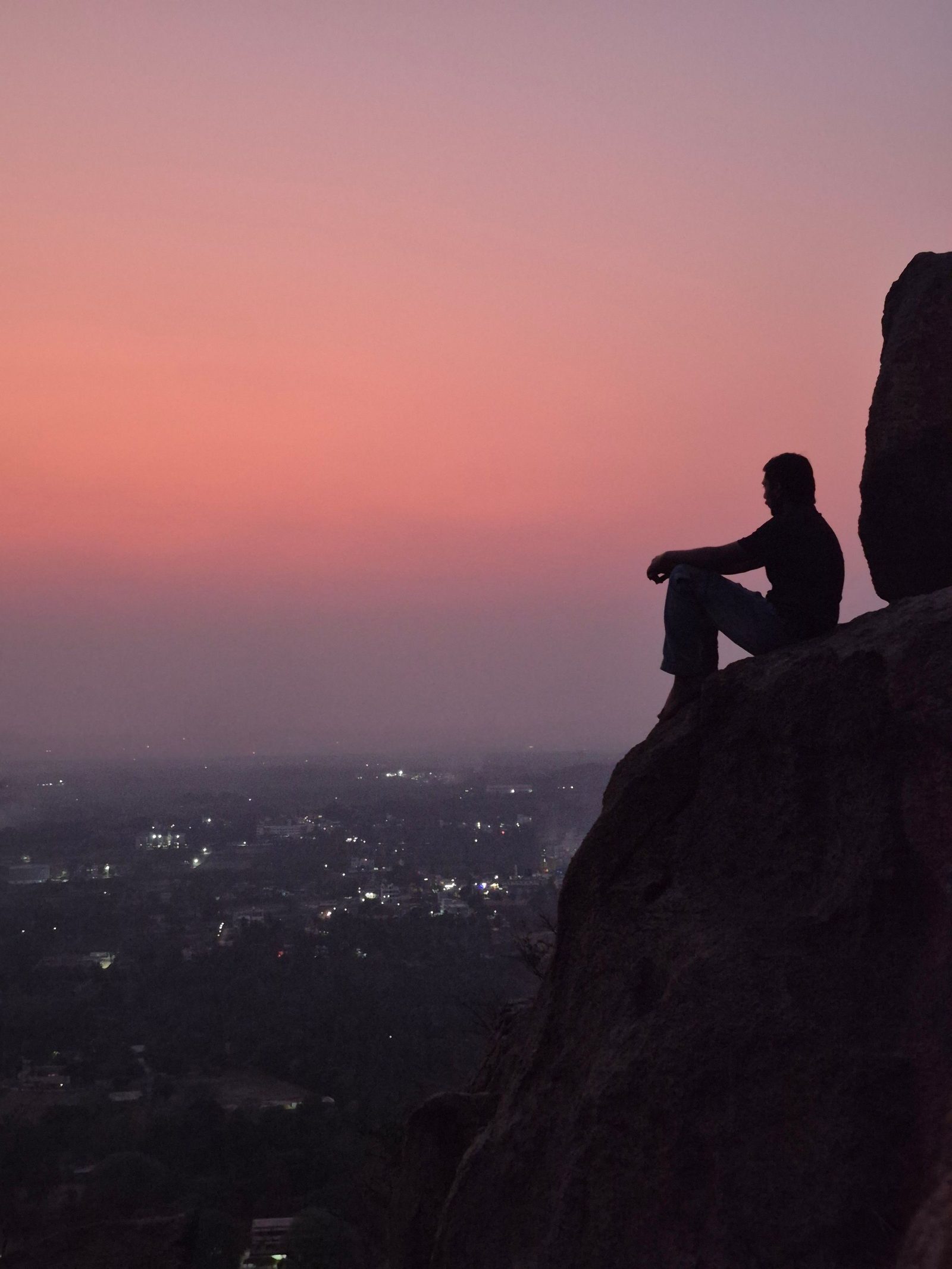 A person sitting alone on a rocky outcrop above Bengaluru at sunset.