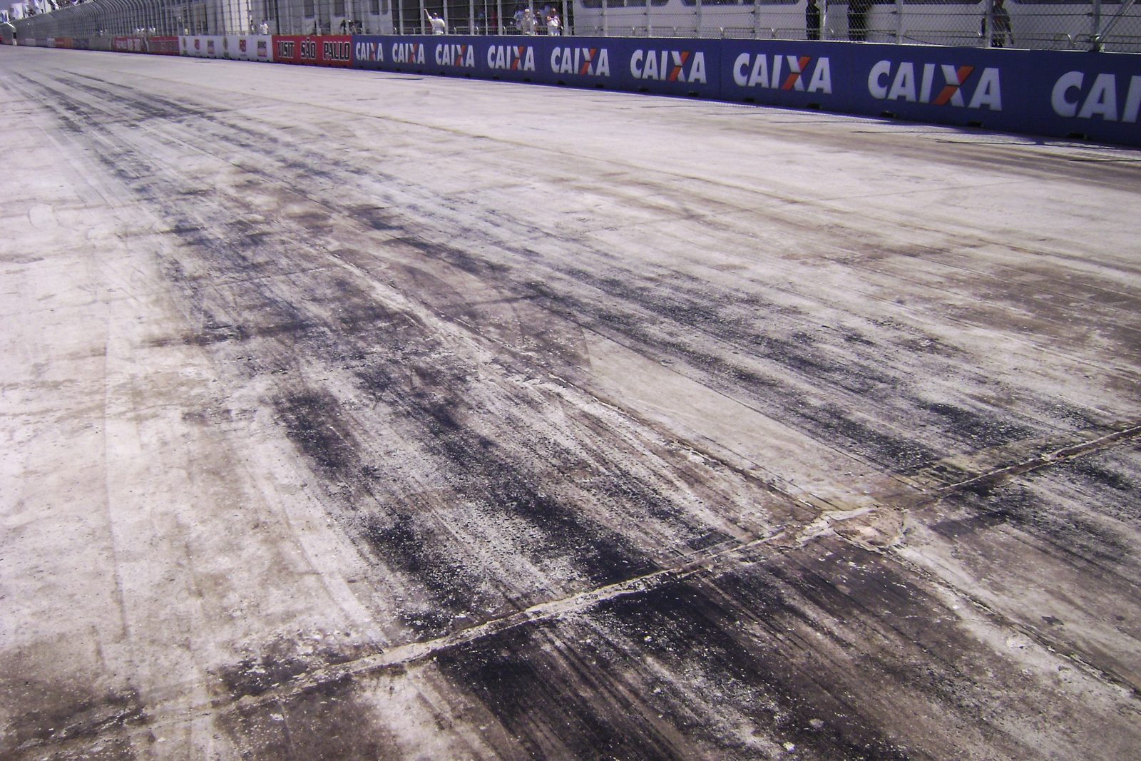 Dark tyre marks laid down on the track at the braking zone at the end of a straight, with grandstands and barriers beside it