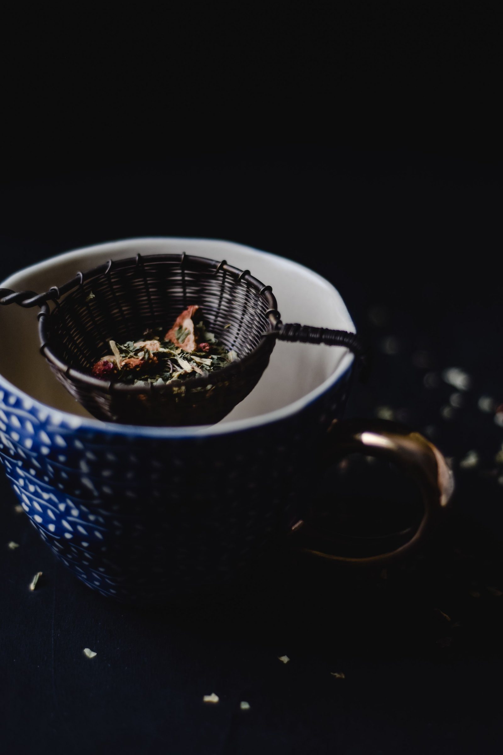 A black tea sieve holding loose leaves sits over a blue ceramic cup.