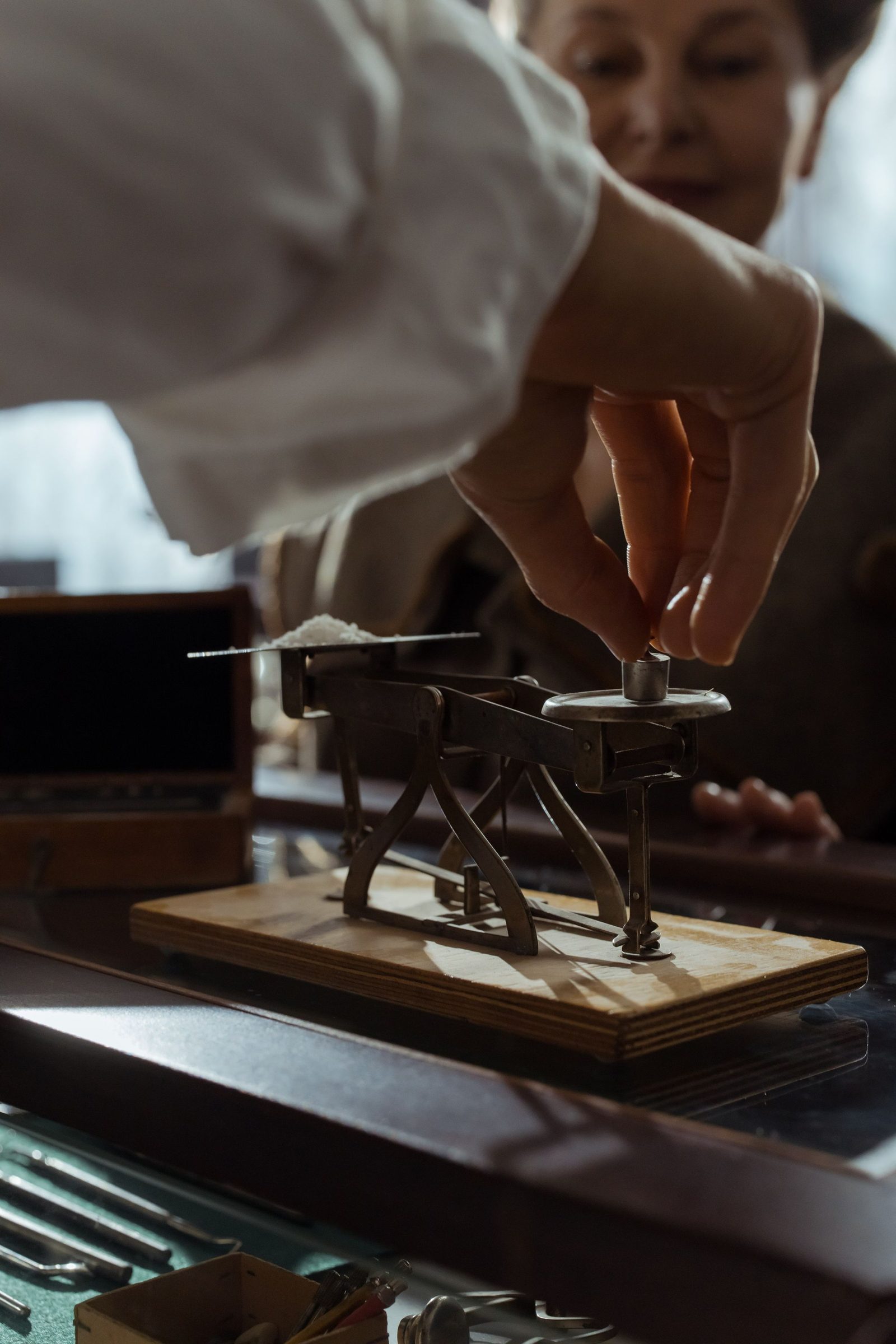 A hand adjusts the weights on an antique brass balance.