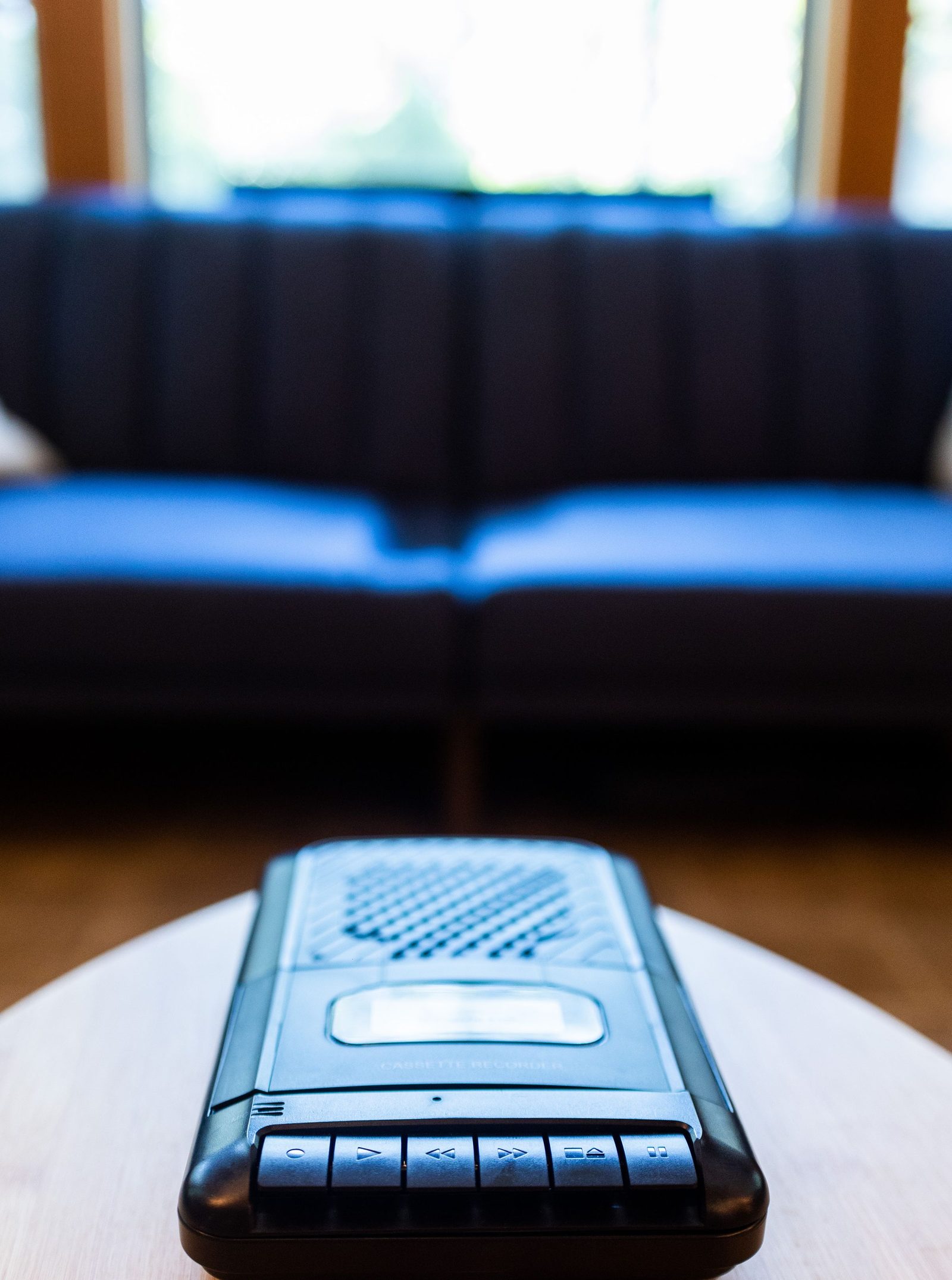 A small black voice recorder lies on a wooden table.