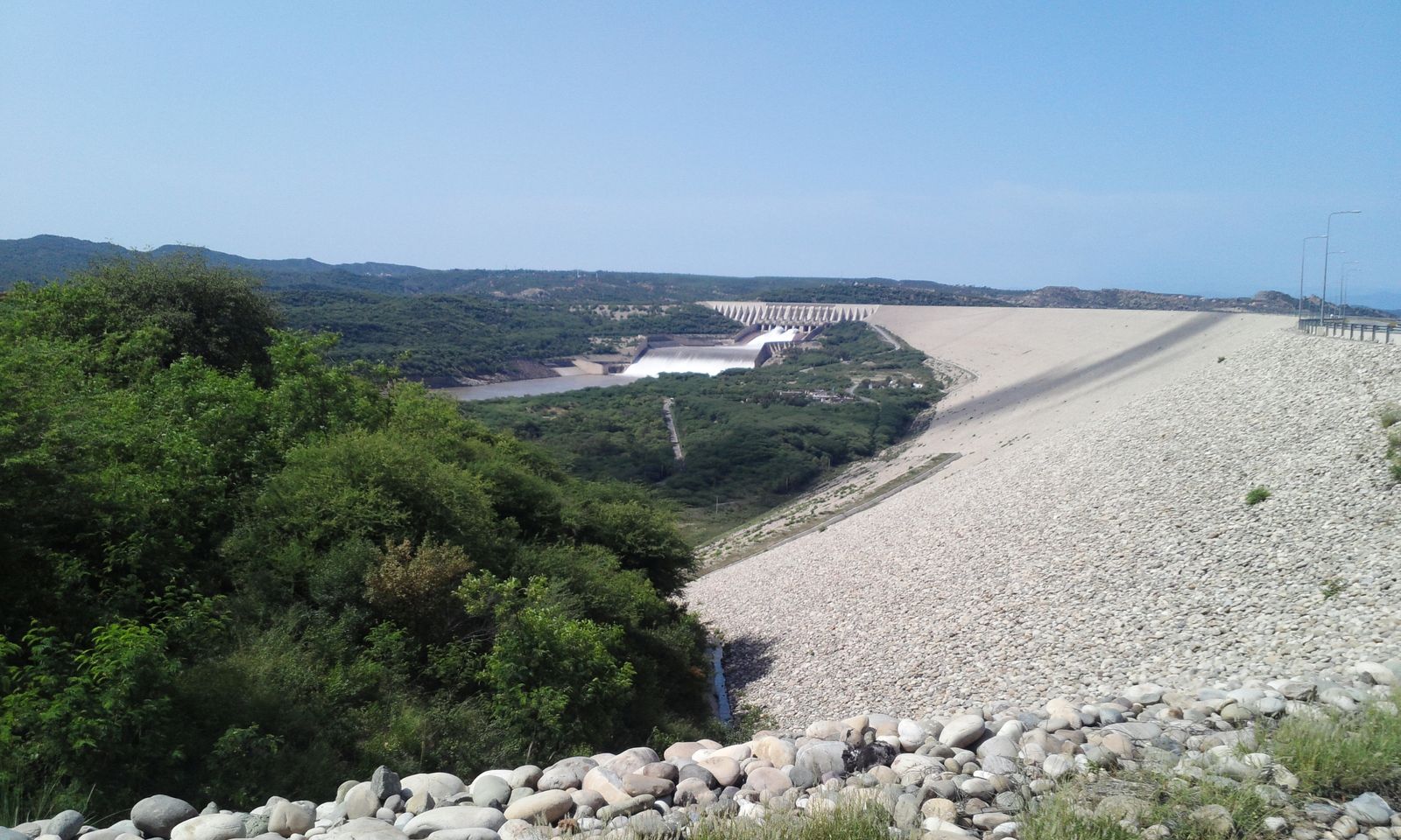 The long stone embankment and spillway of Mangla Dam under a clear sky