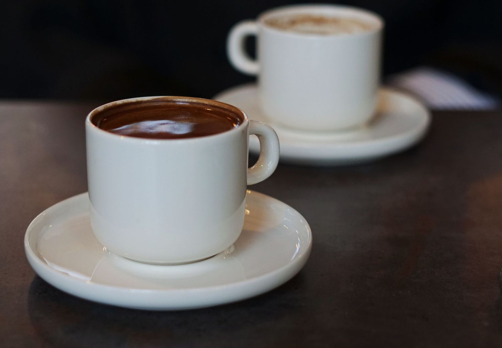 Two white cups of coffee on saucers on a café table