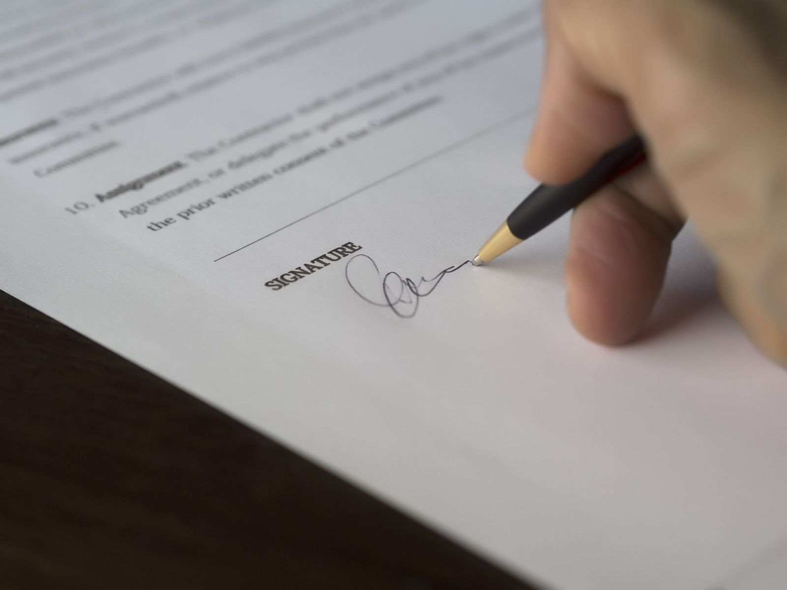 A hand signing a printed agreement with a pen on a wooden desk