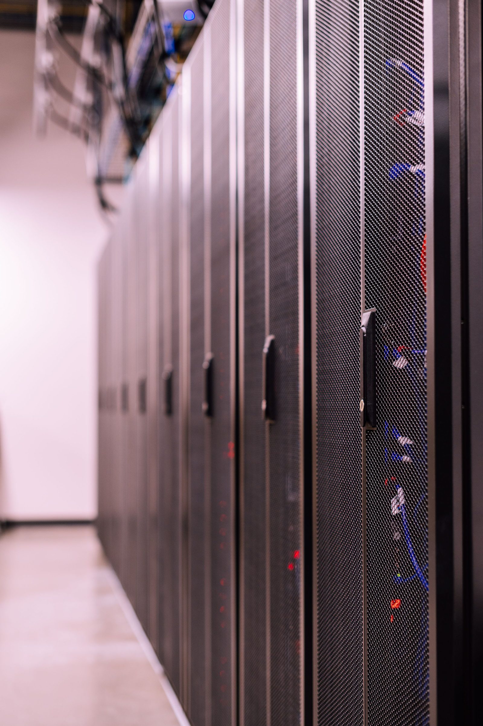 Rows of black server racks with optical fibre cables in a data centre.