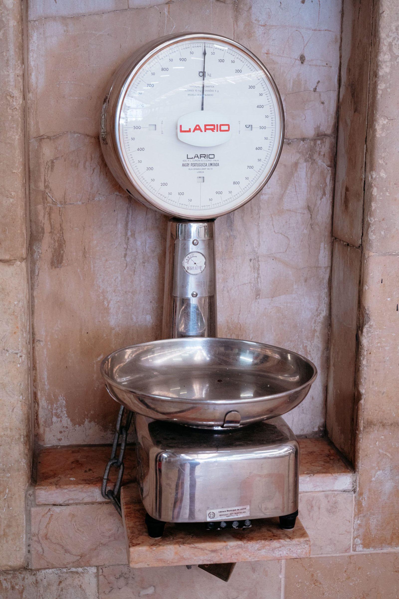 A vintage analogue weighing scale with a metal bowl against a rough wall.