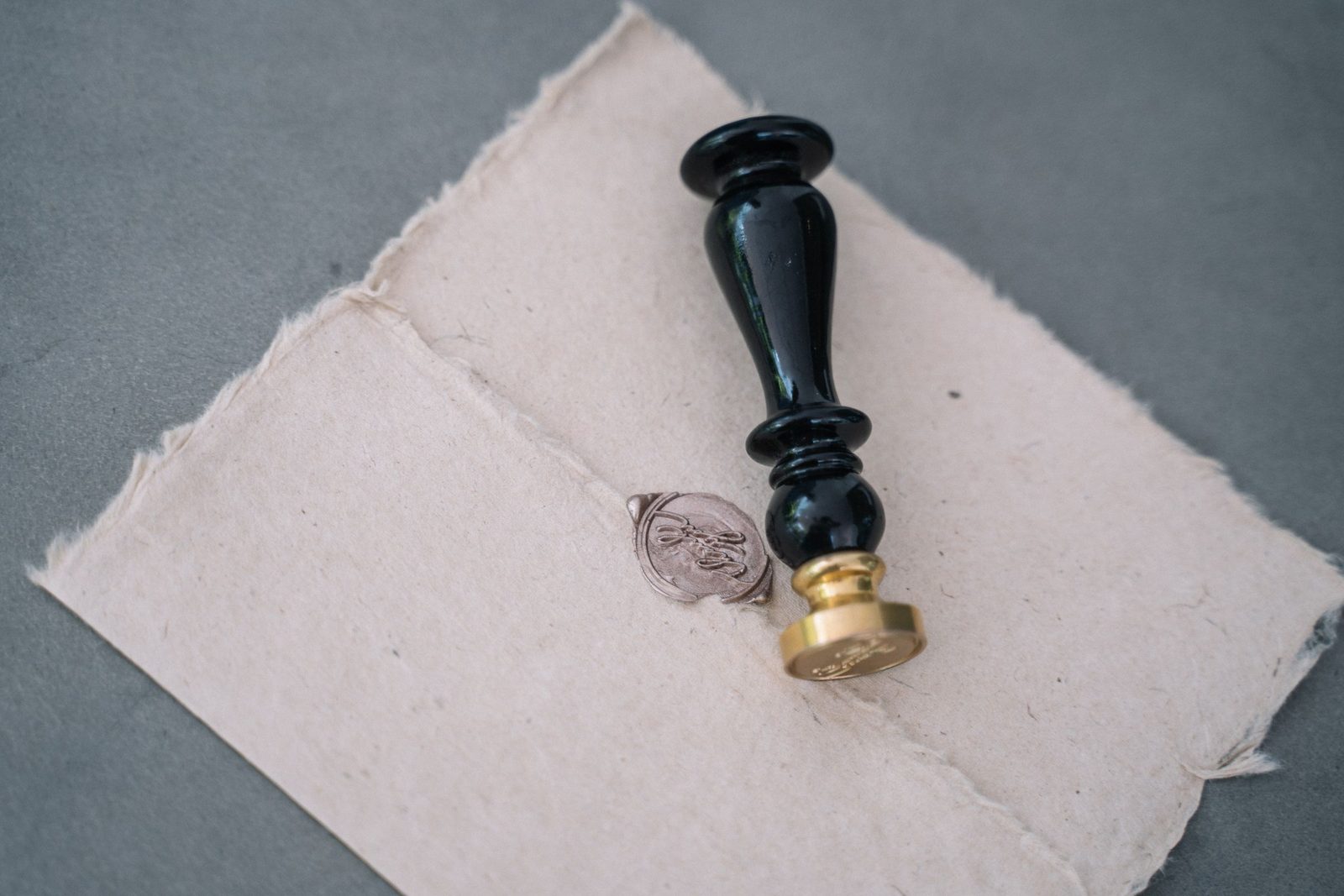 A black-handled brass seal beside a silver wax seal on folded handmade paper