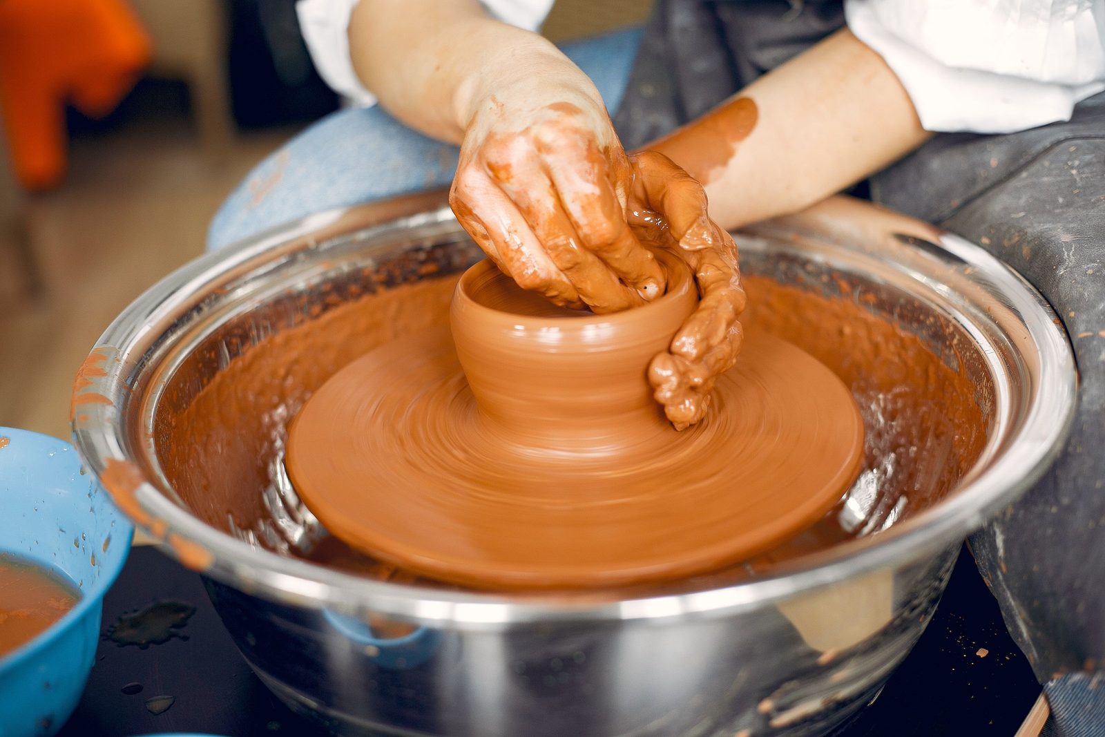 A ceramist in an apron shapes clay on a potter's wheel in a studio.