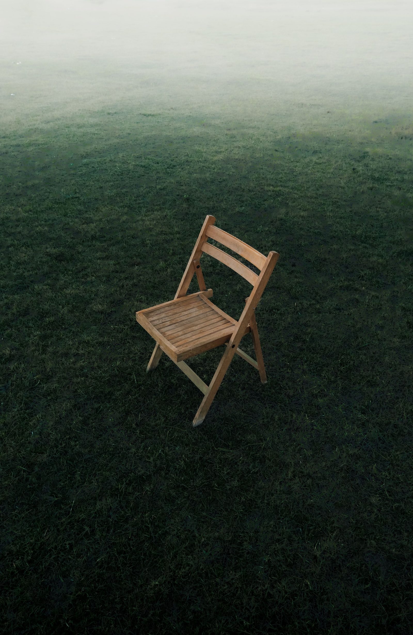 A single wooden chair stands on a misty grass field.