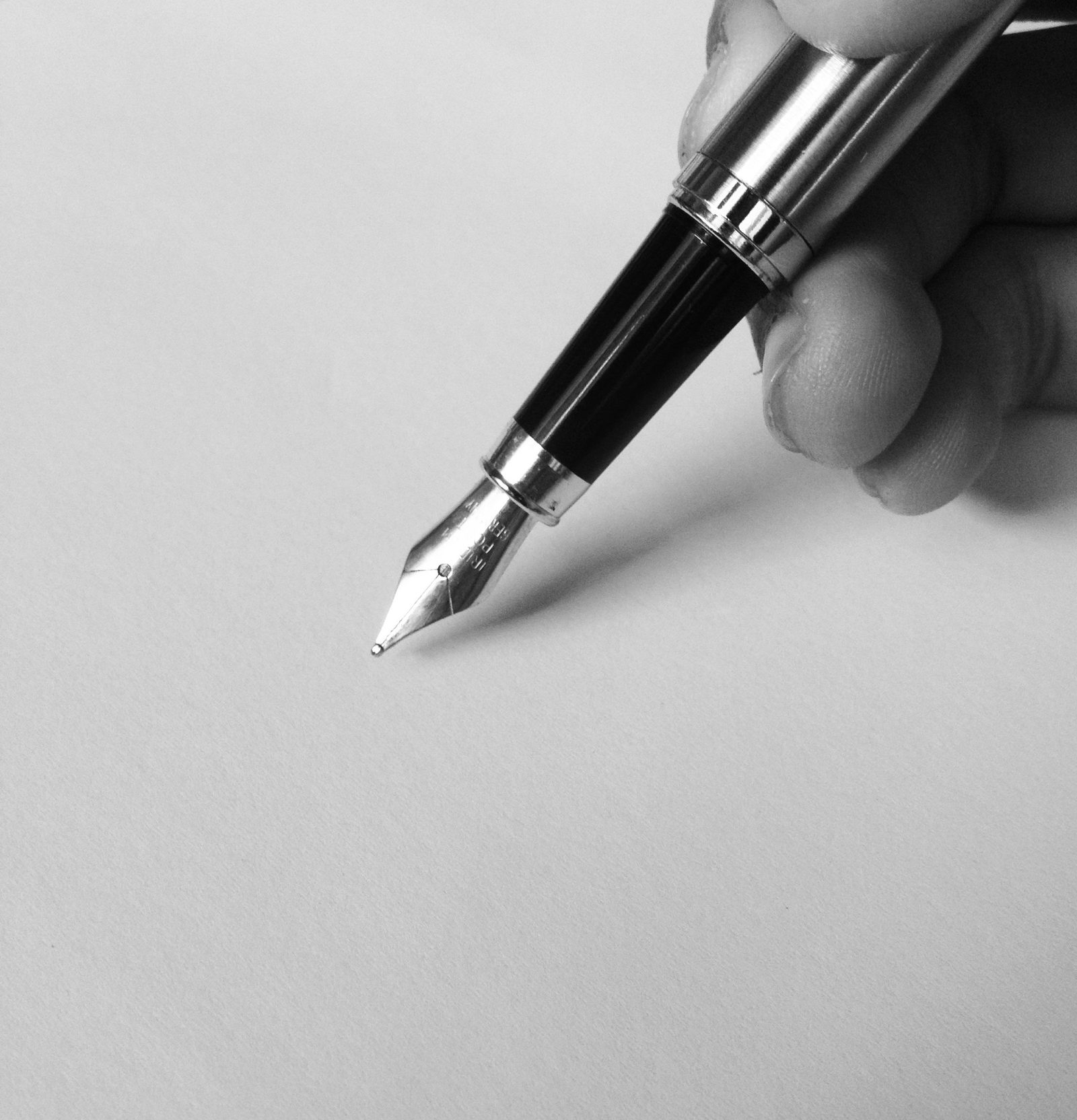 A fountain pen touches a blank sheet of paper in black and white.